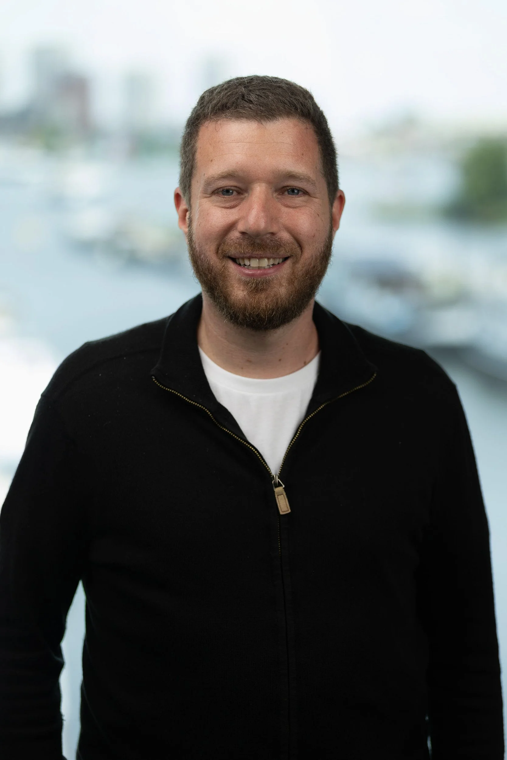 Bearded male professional headshot in black jacket with Amsterdam waterfront background — business portrait photography Amsterdam Ballo Studio