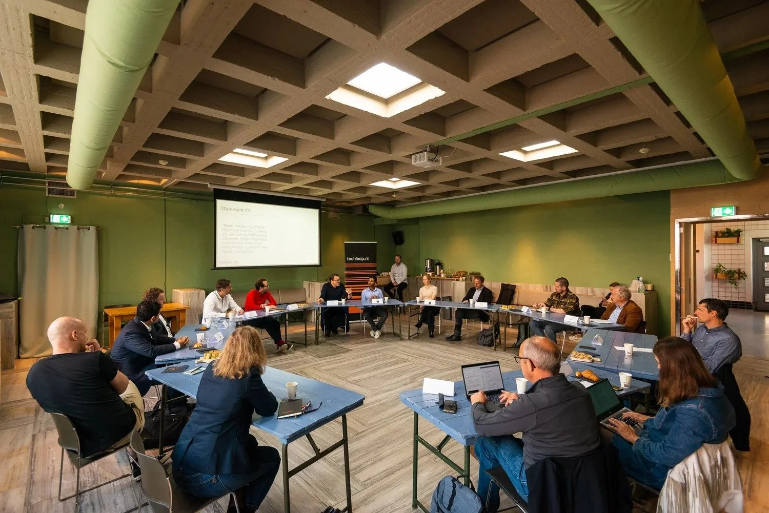 Corporate workshop attendees seated in round-table format with presentation screen — conference photography Ballo Studio