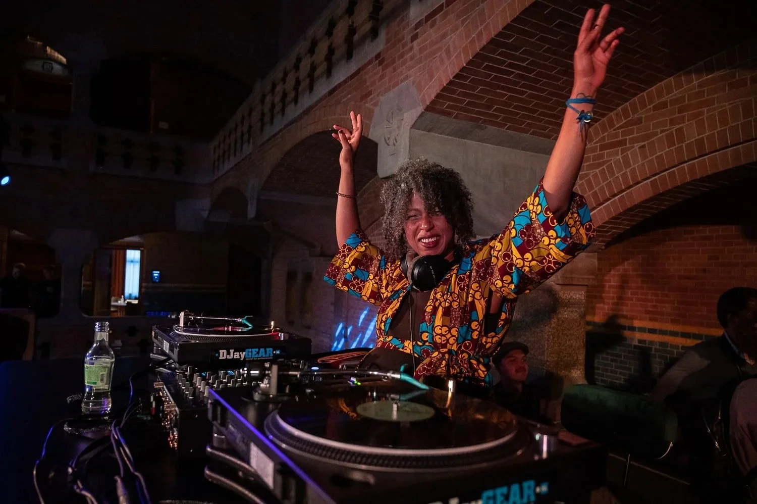 Female DJ with arms raised performing at decks in brick-arched venue at corporate event party Amsterdam — corporate event photography Amsterdam Ballo Studio
