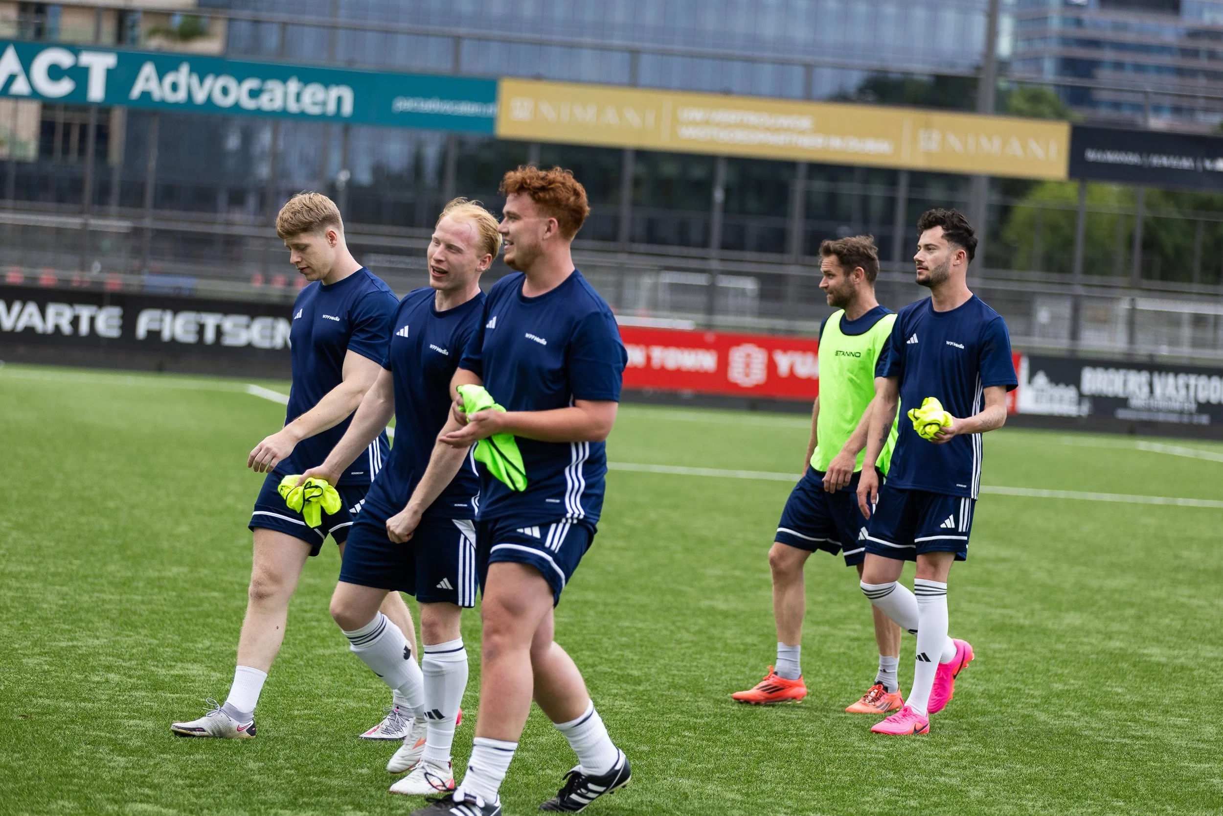Football team in dark blue kit walking onto pitch at Adfocup 2026 advertising industry tournament Amsterdam — corporate event photography Amsterdam Ballo Studio