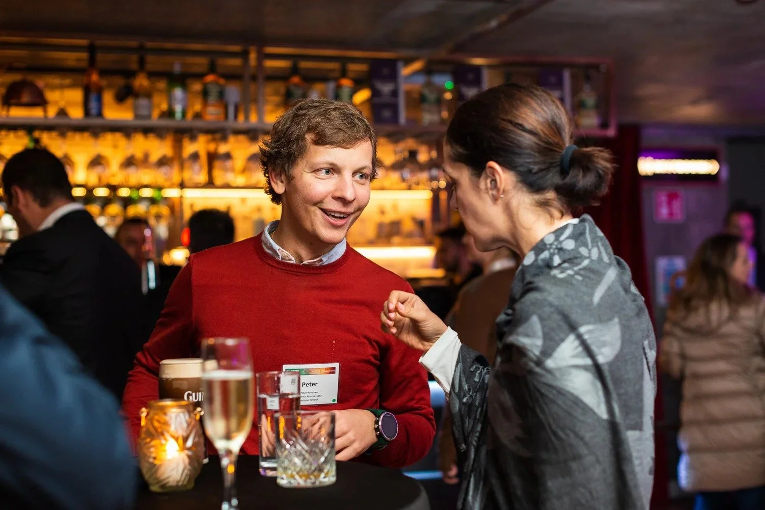 Delegate in red sweater chatting and laughing at bar during corporate conference networking drinks Amsterdam — event photography Amsterdam Ballo Studio