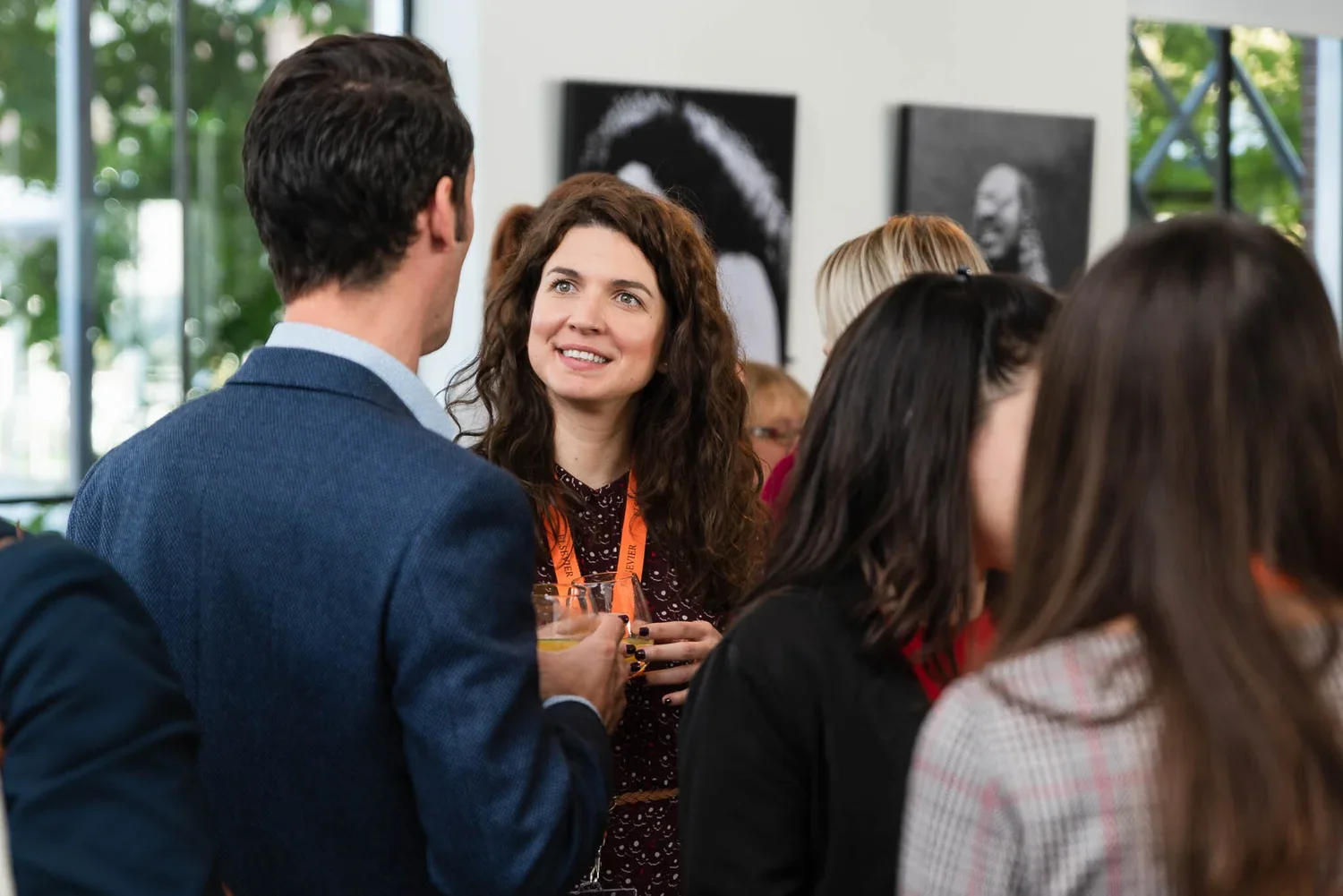 People at a social gathering, engaging in conversation, in an indoor setting with artwork on the wall.