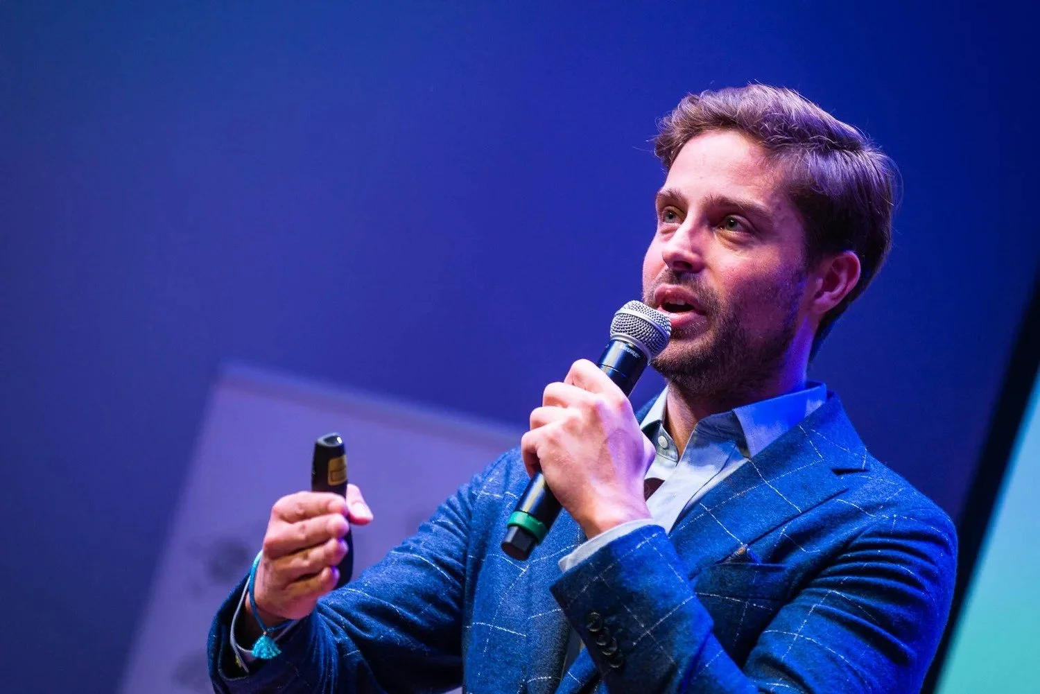 Male speaker in blue blazer with microphone presenting at corporate conference against blue-lit stage background Amsterdam — conference photography Amsterdam Ballo Studio