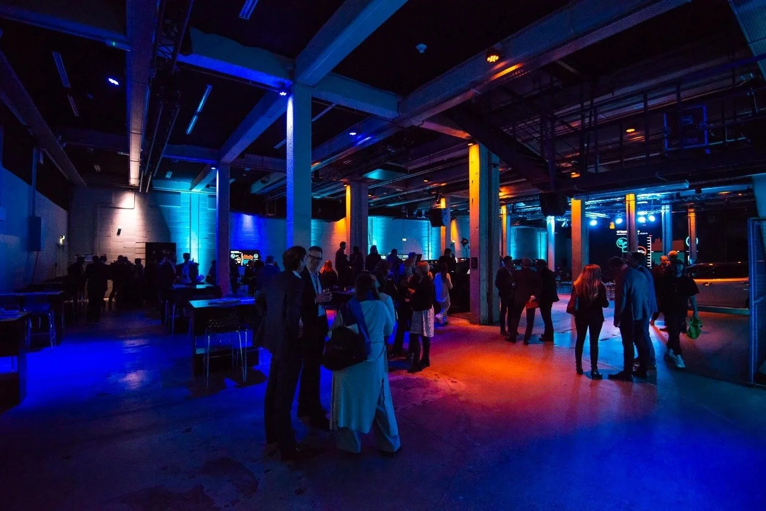 Guests mingling in dramatic industrial event venue with blue and amber lighting at corporate networking reception Amsterdam — event photographer Amsterdam Ballo Studio