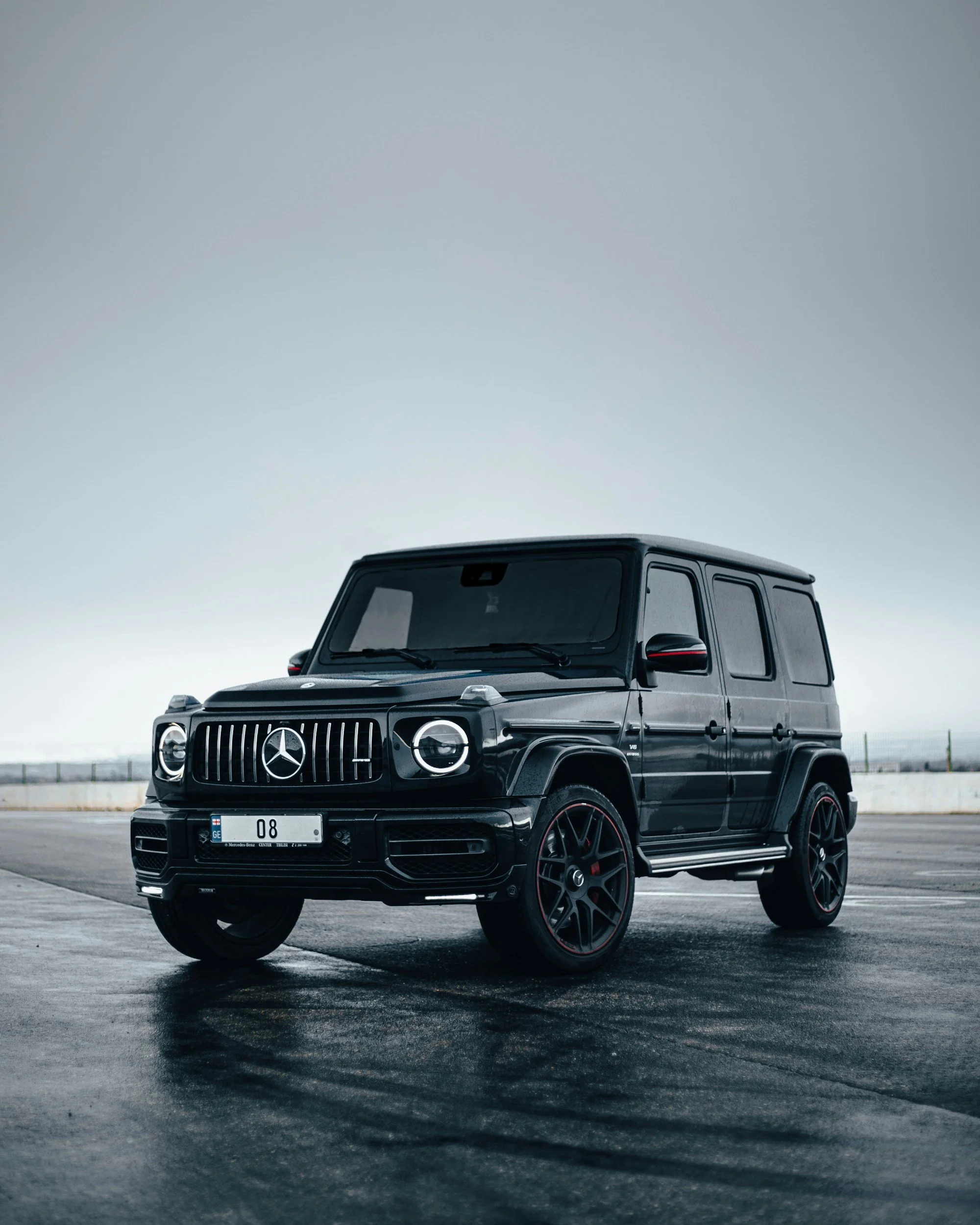 A black Mercedes-Benz G-Class SUV parked on wet asphalt on a cloudy day.