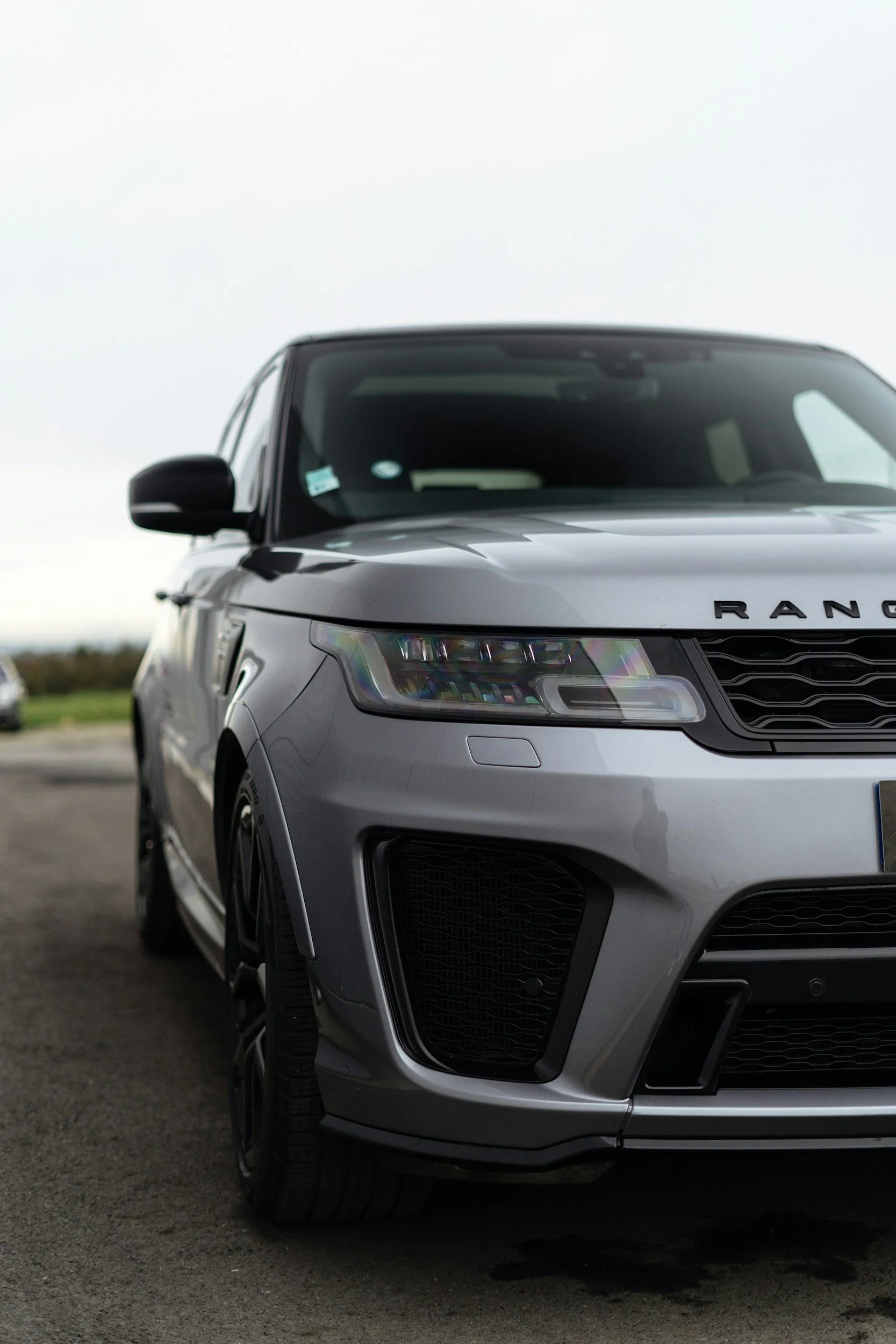 Close-up of a silver Range Rover SUV parked on a road, showing the front and driver side of the vehicle.