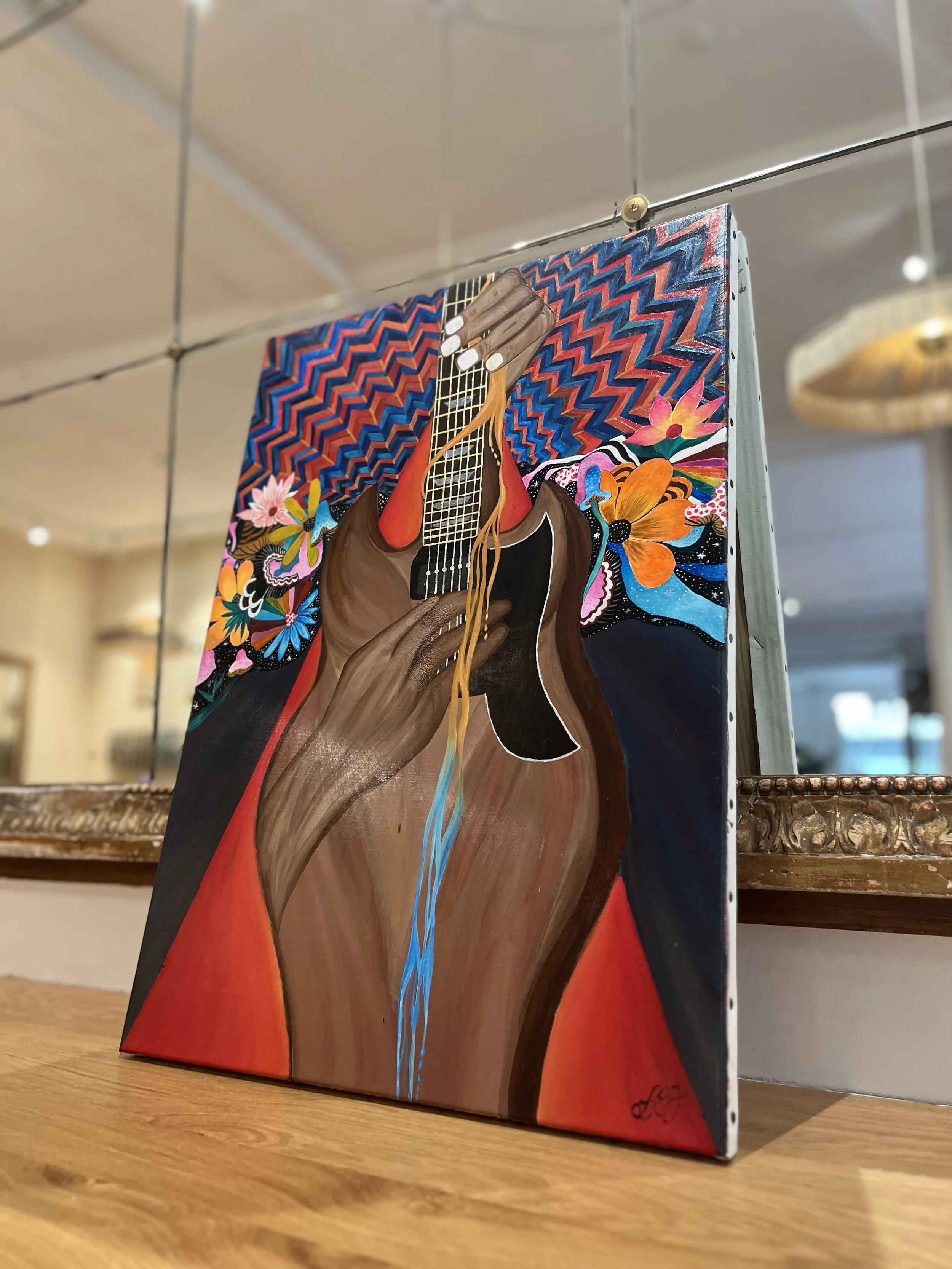 Une peinture représentant une main jouant de la guitare, entourée de fleurs colorées et d'un fond avec un motif en zigzag de couleurs vives.