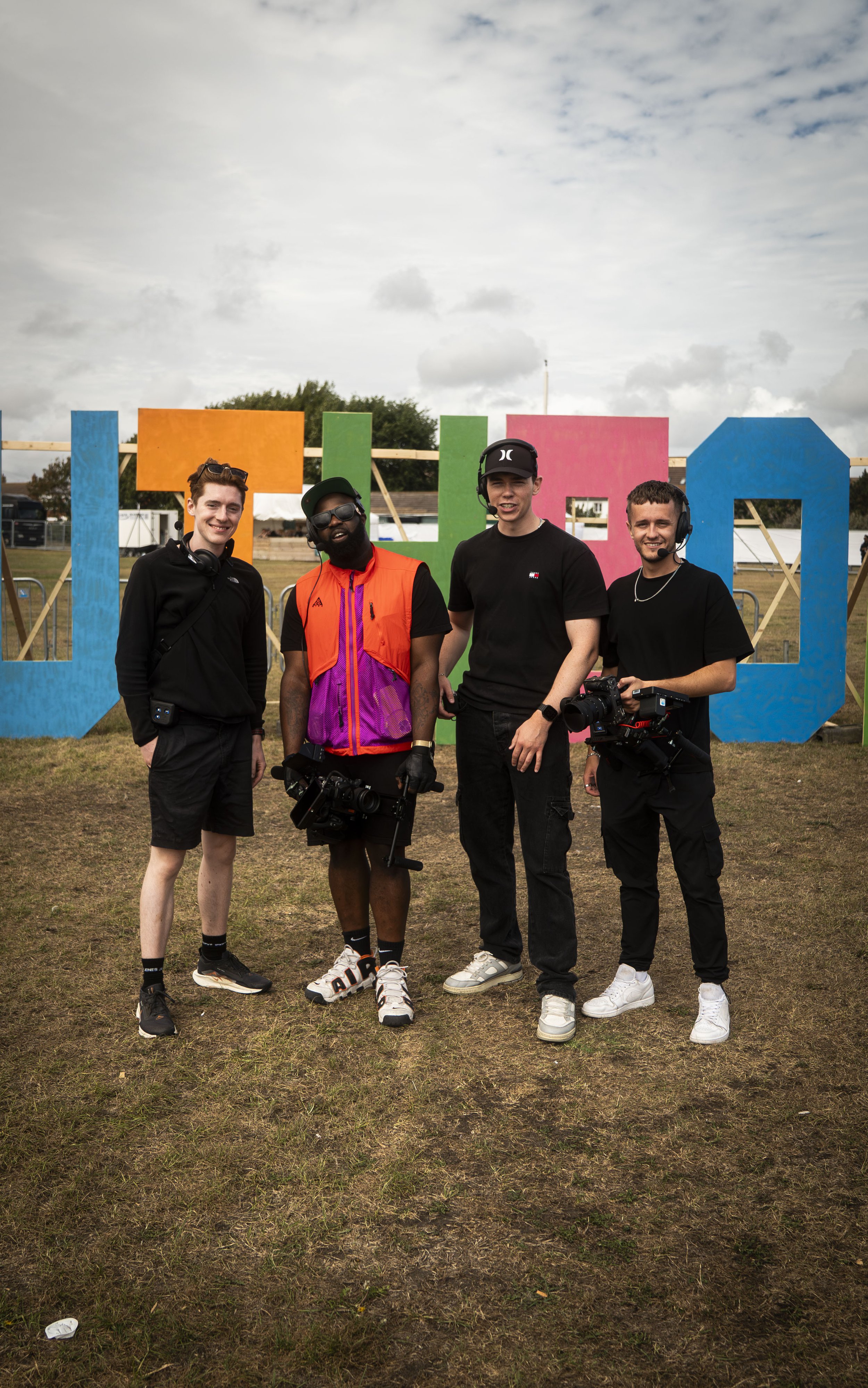Four young men posing outdoors in front of large, colorful letters. The videography team for a music festival.