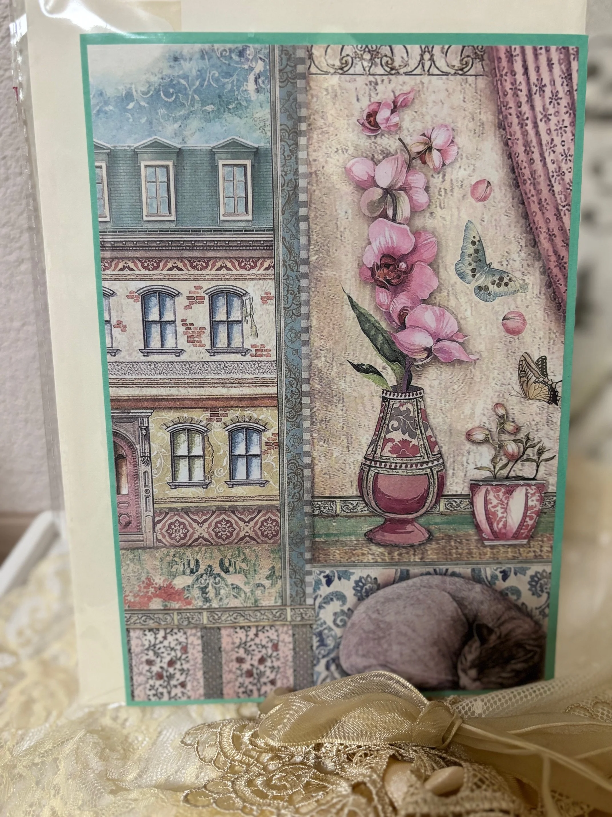 Schön gestaltete Collage mit einem Gebäude, einer Vase mit pinken Blumen, einer Pflanze in einer kleinen Tontopf und einem schlafenden braun-grauen Kater auf einem Teppich.