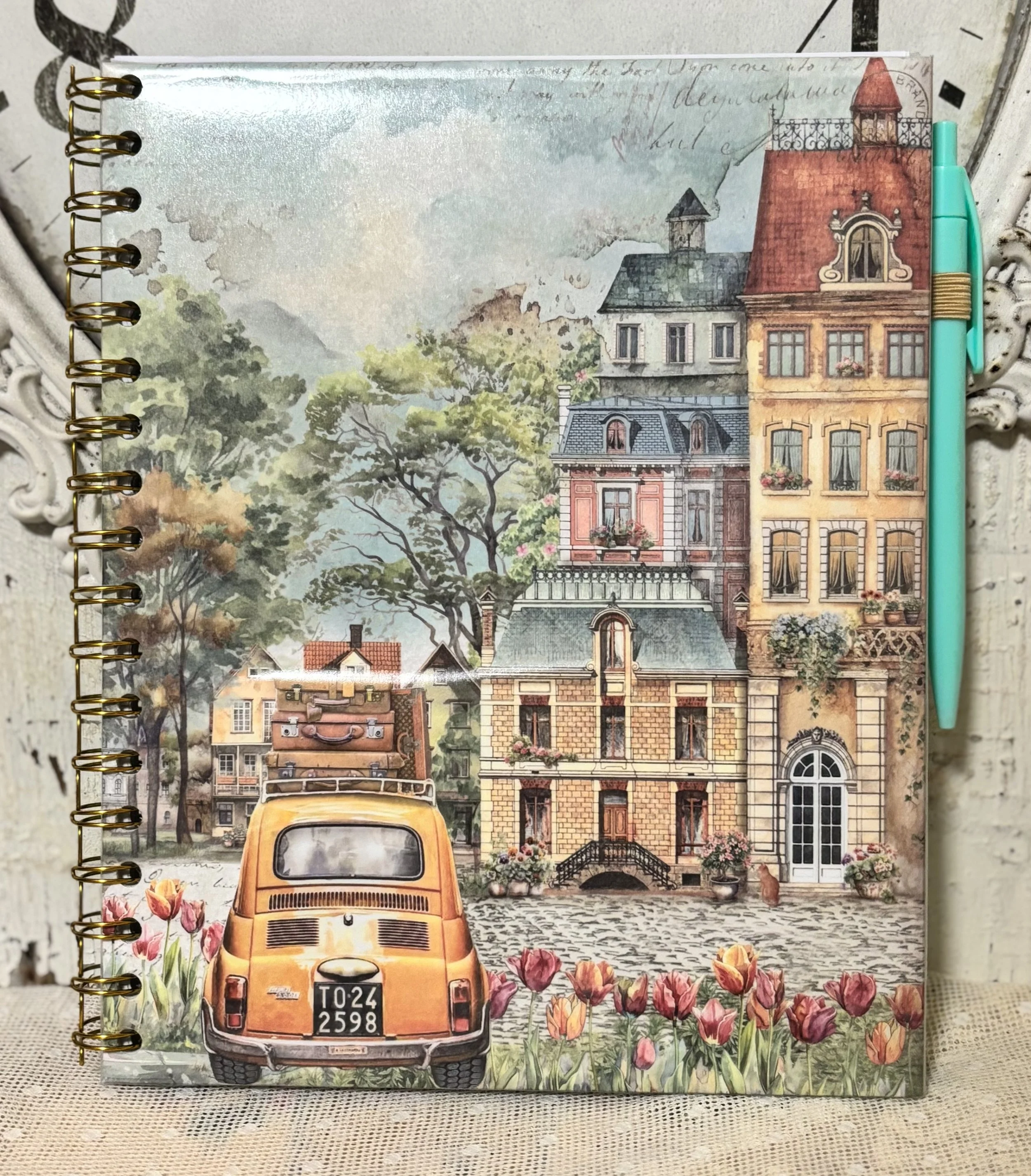 Illustration eines europäischen Stadtbildes mit alten Gebäuden, einem auffälligen orangefarbenen Auto im Vordergrund, Blumen im Garten und Bäumen im Hintergrund.