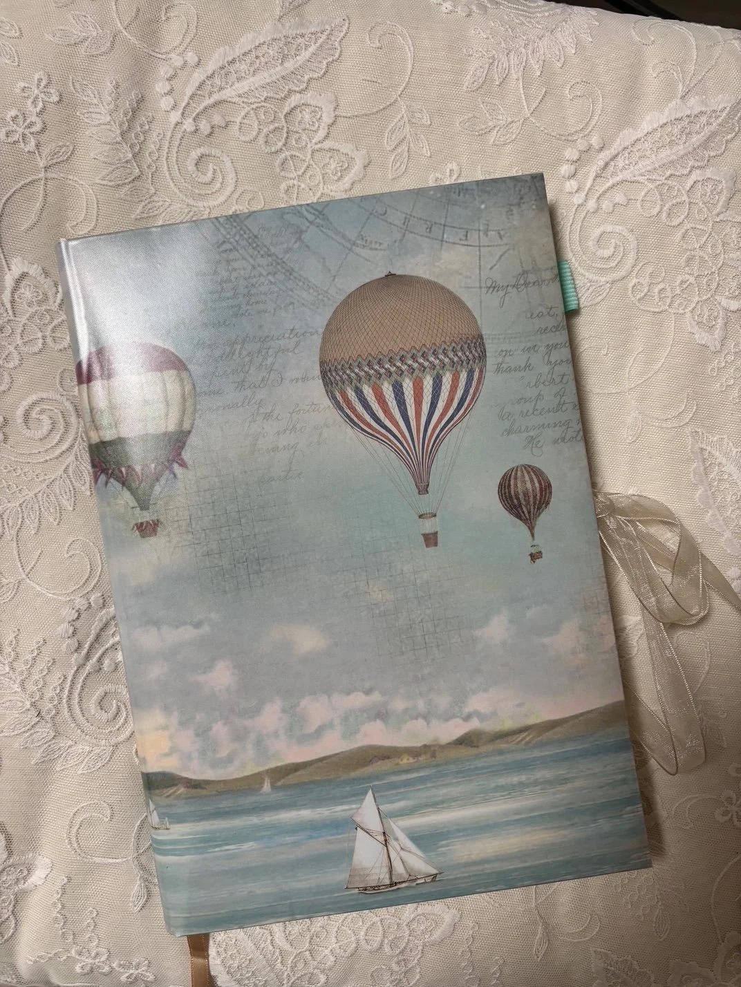 Ein Notizbuch mit einem Himmel- und Ballonmotiv, das auf einem gewebten, verzierenden Tischler liegt.