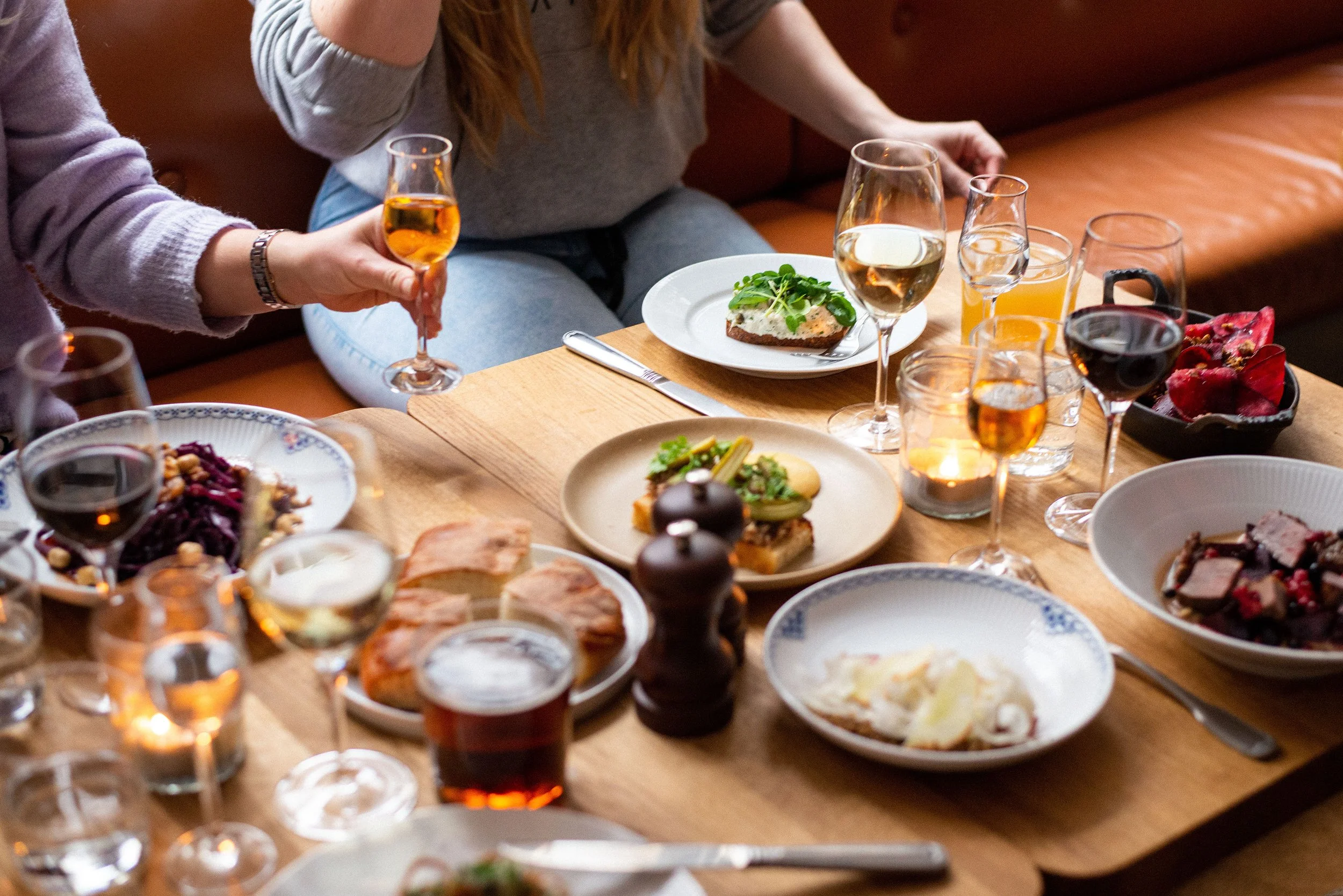 Et bord med forskellige retter og drinks, hvor nogle mennesker holder glas