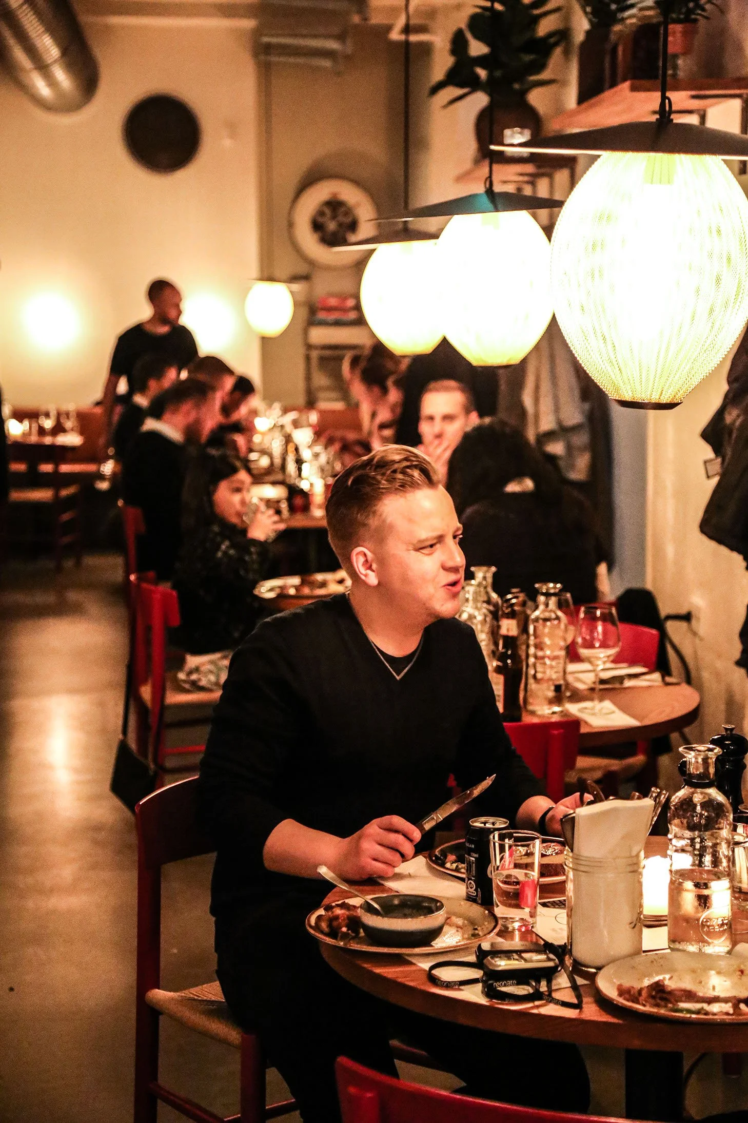 Mennesker, der spiser og hygger sig i en hyggelig restaurant med varme lys og moderne dekoration.