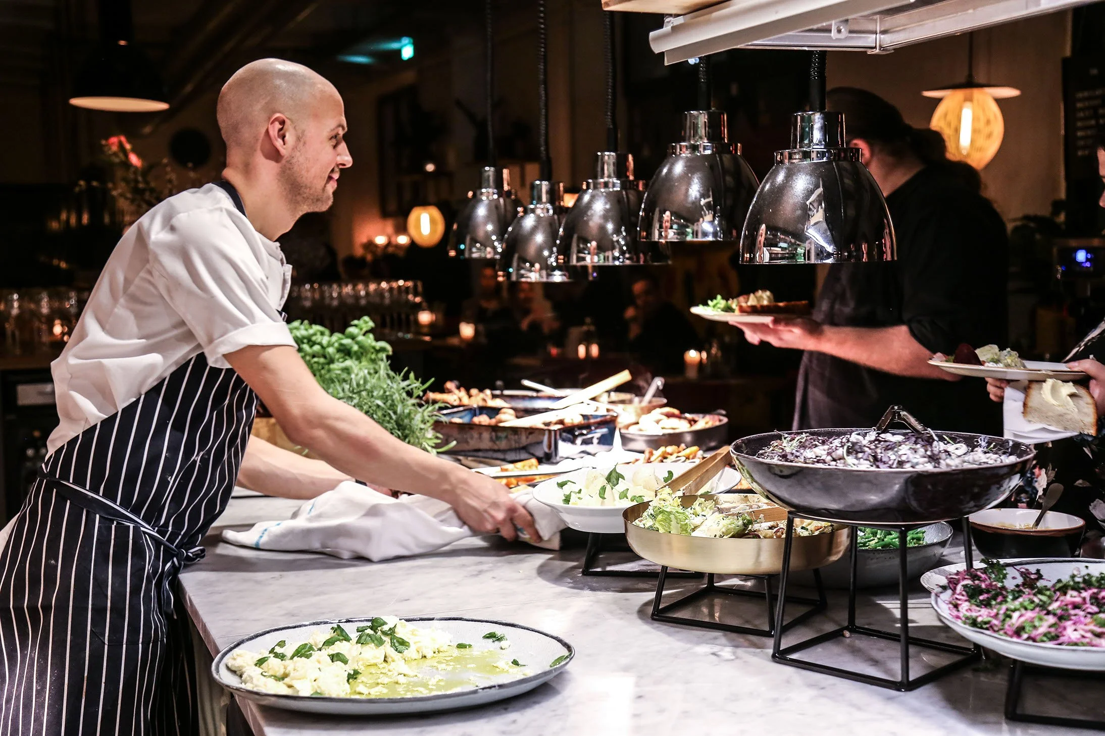 En kok i en restaurant serverer en buffet med salater og retter.