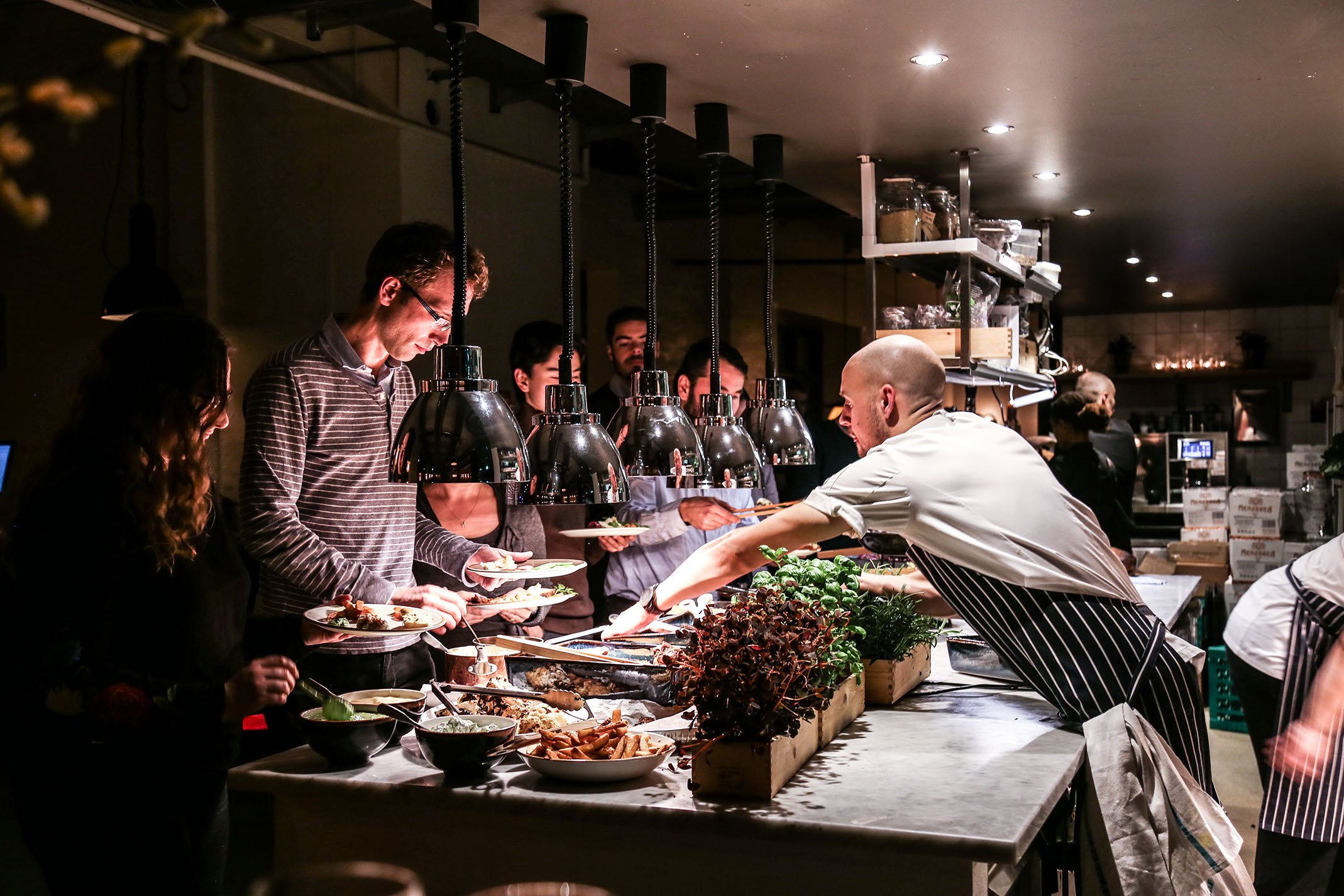 Køkkenpersonale serverer mad til gæster ved en buffet i en restaurant.