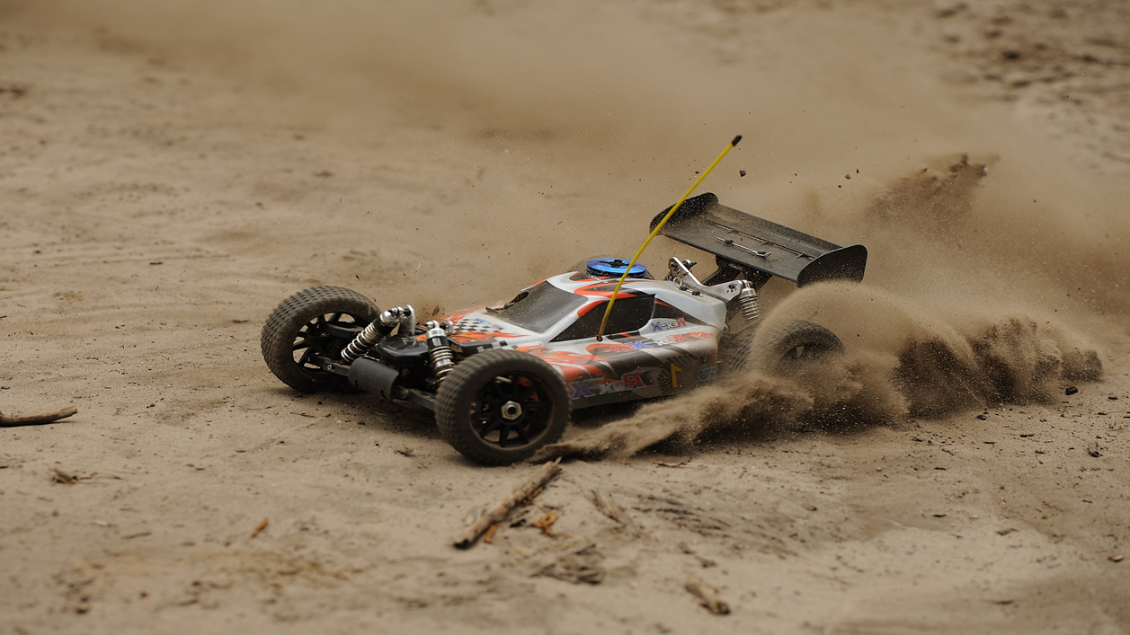 En RC-bil kører i sandet, hvilket får sand til at flyve op bag den.
