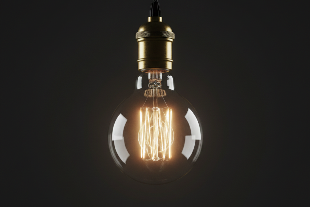A lit incandescent light bulb with a glowing filament against a dark background.