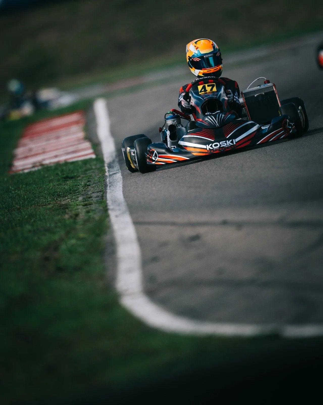 Go-kart racing on a racetrack with the driver in racing suit and helmet maneuvering through a turn.