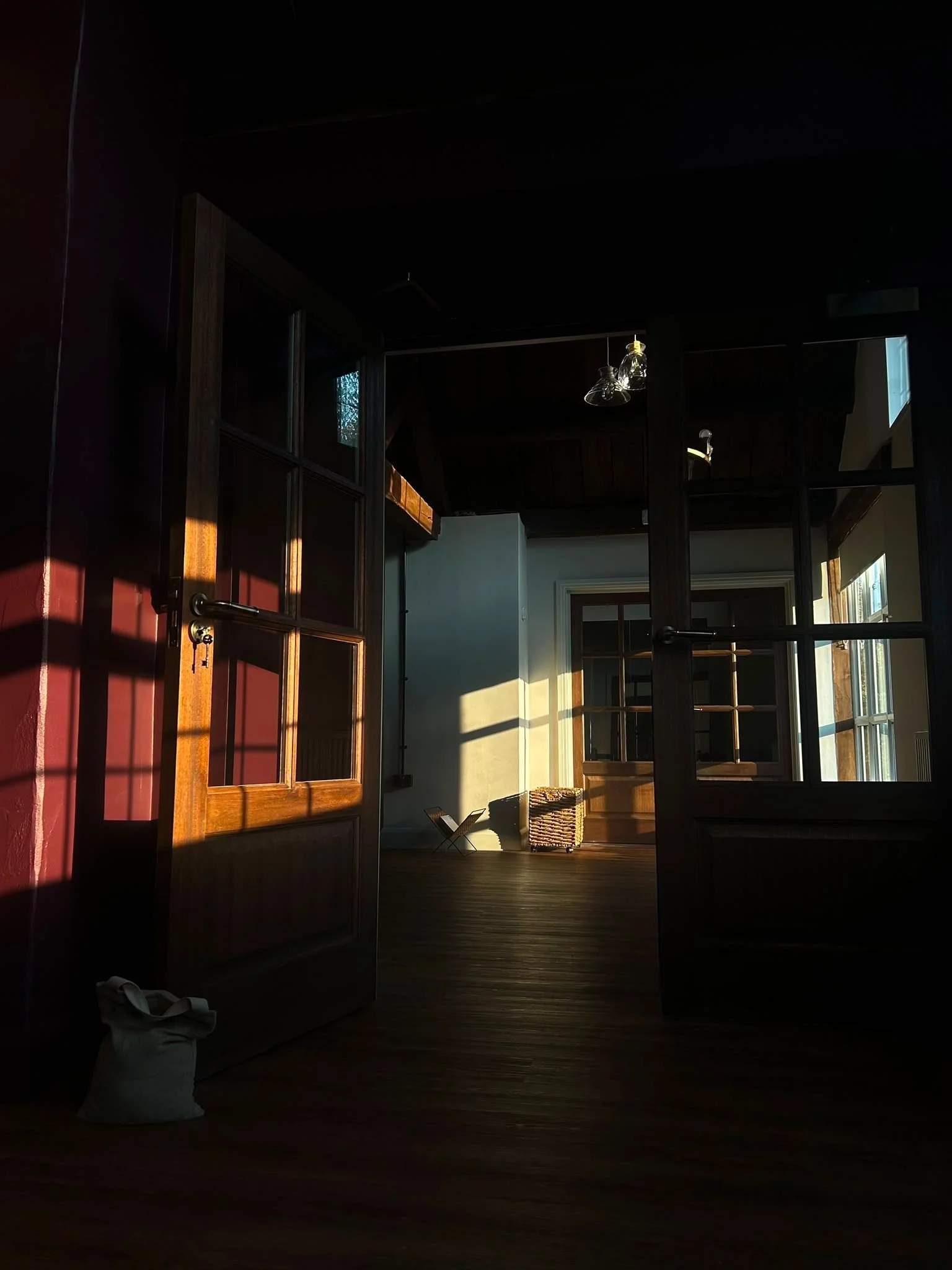 Sunlight streaming into a room through glass-paned wooden doors, illuminating the farmhouse lounge.