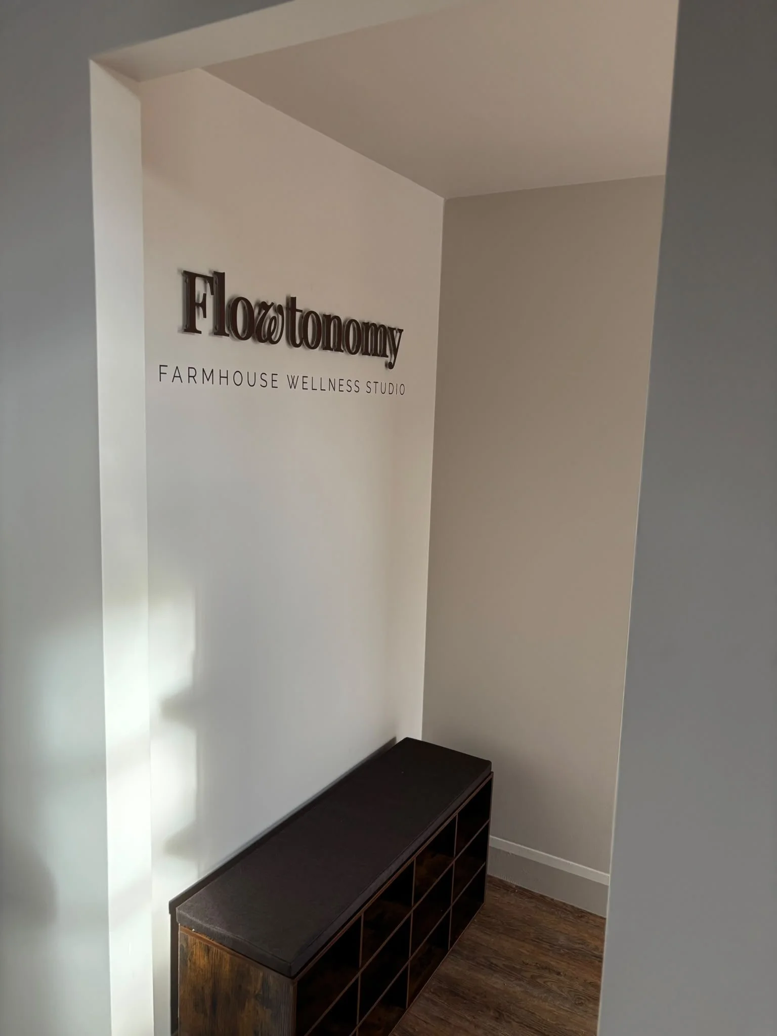 Interior of a wellness studio with a wall sign that reads 'Flotonomy Farmhouse Wellness Studio' and a dark wooden cabinet below.