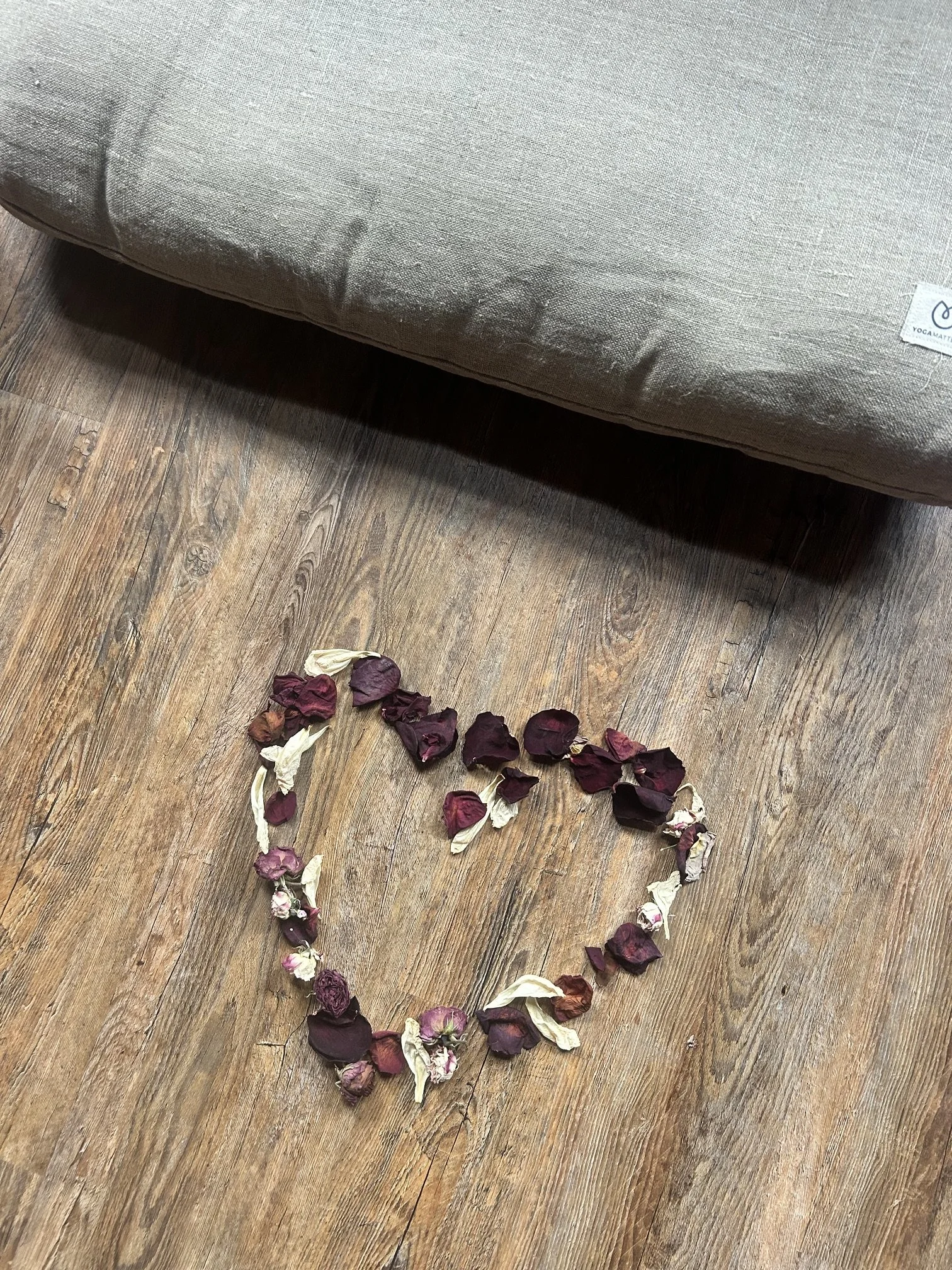 Dried rose petals arranged in a heart shape on wooden floor next to a yoga mat.