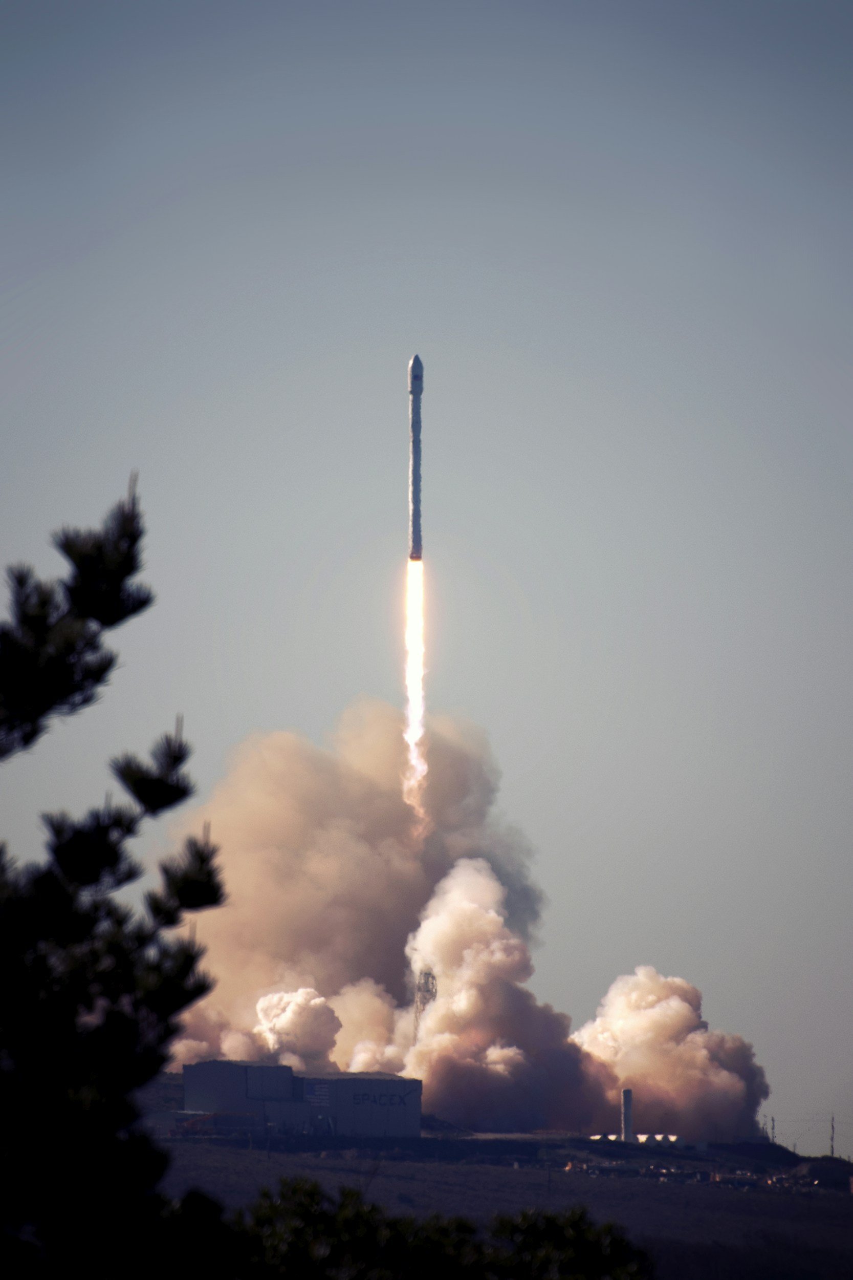 Rocket launching into the sky with a trail of smoke and fire, surrounded by some trees in the foreground.