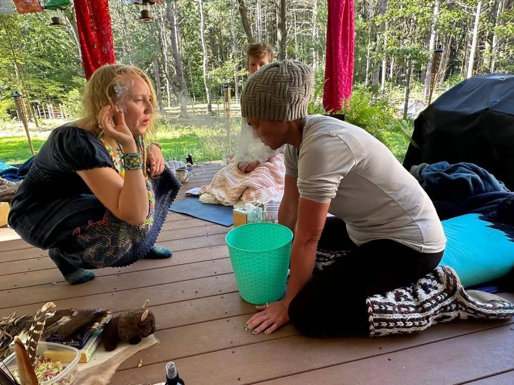 Kambo ceremony in progress with participant seated beside a green bucket, supported by practitioner in an outdoor setting.