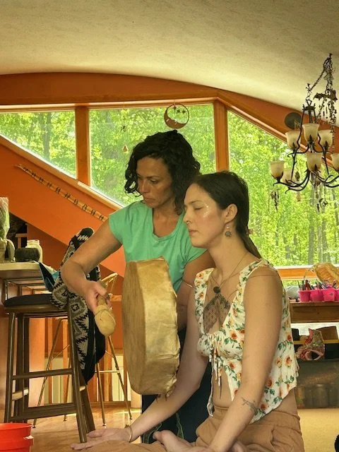 Heather Dexter supporting participant during Kambo ceremony while playing a handheld drum.
