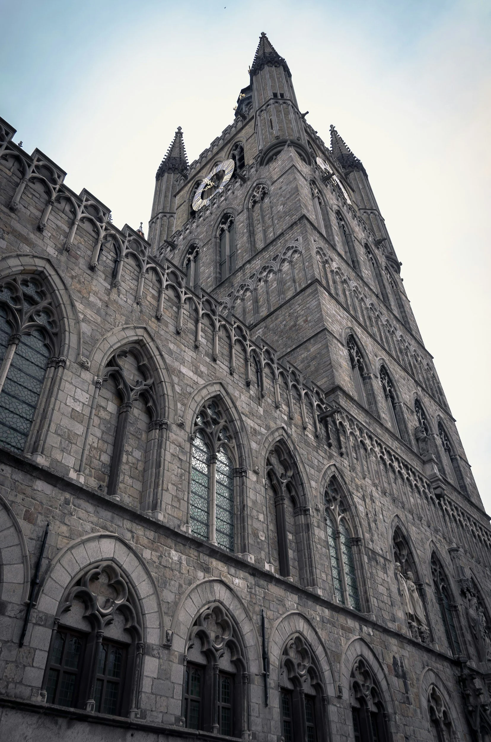 A low-angle view of a historic gothic-style stone church with tall, ornate windows and a prominent clock on the tower.