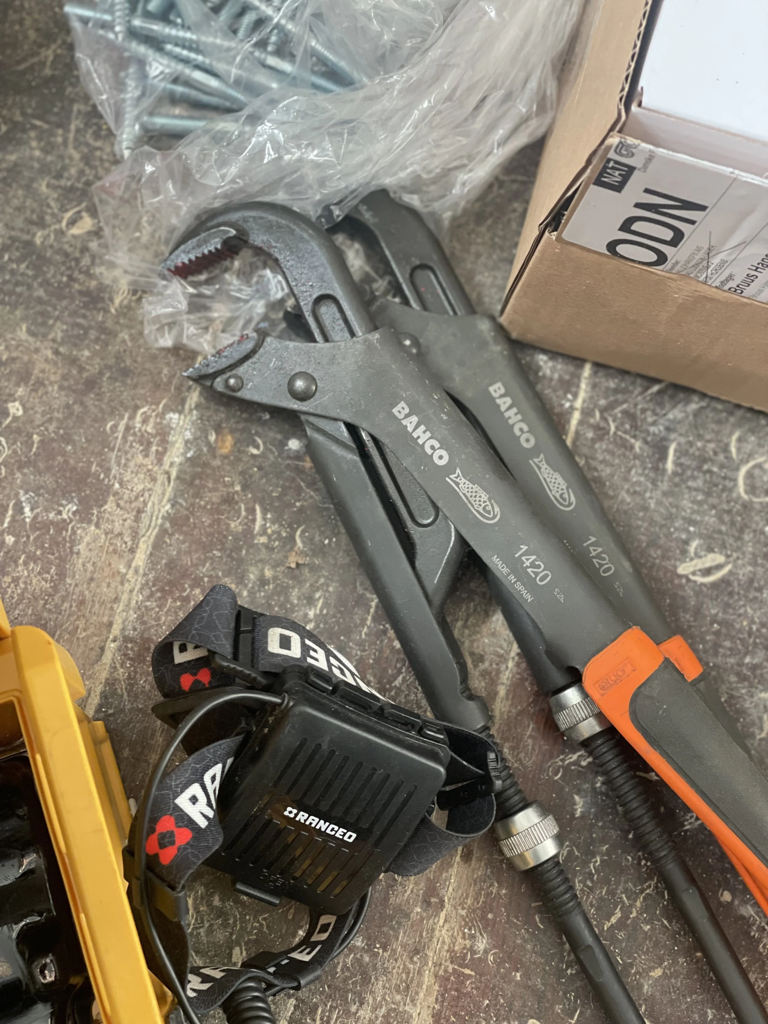 A pair of Bahco hand clamps, a headlamp, a box of brushes, and a yellow tool are on a wooden work surface.