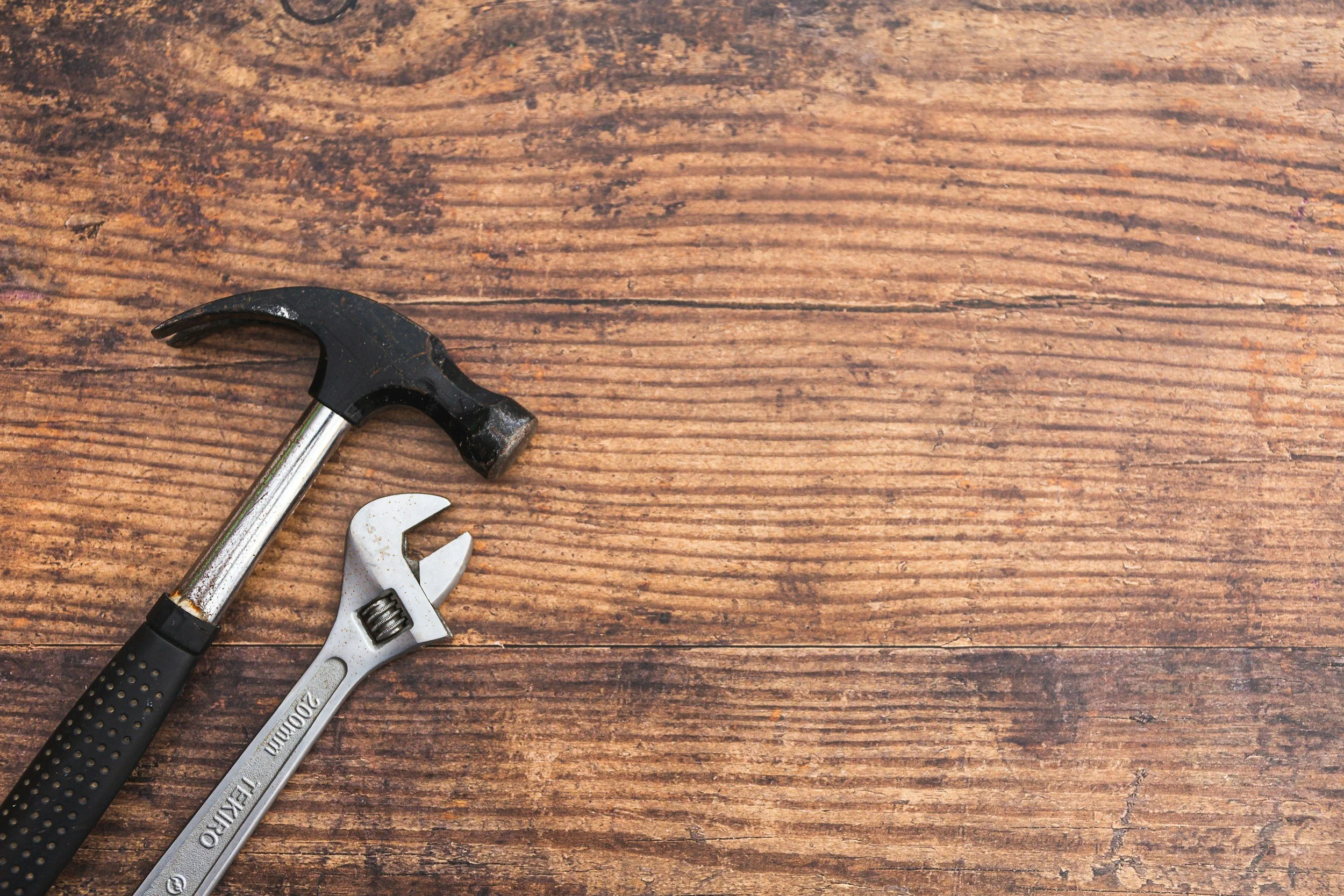 Hammer and adjustable wrench on a wooden surface.