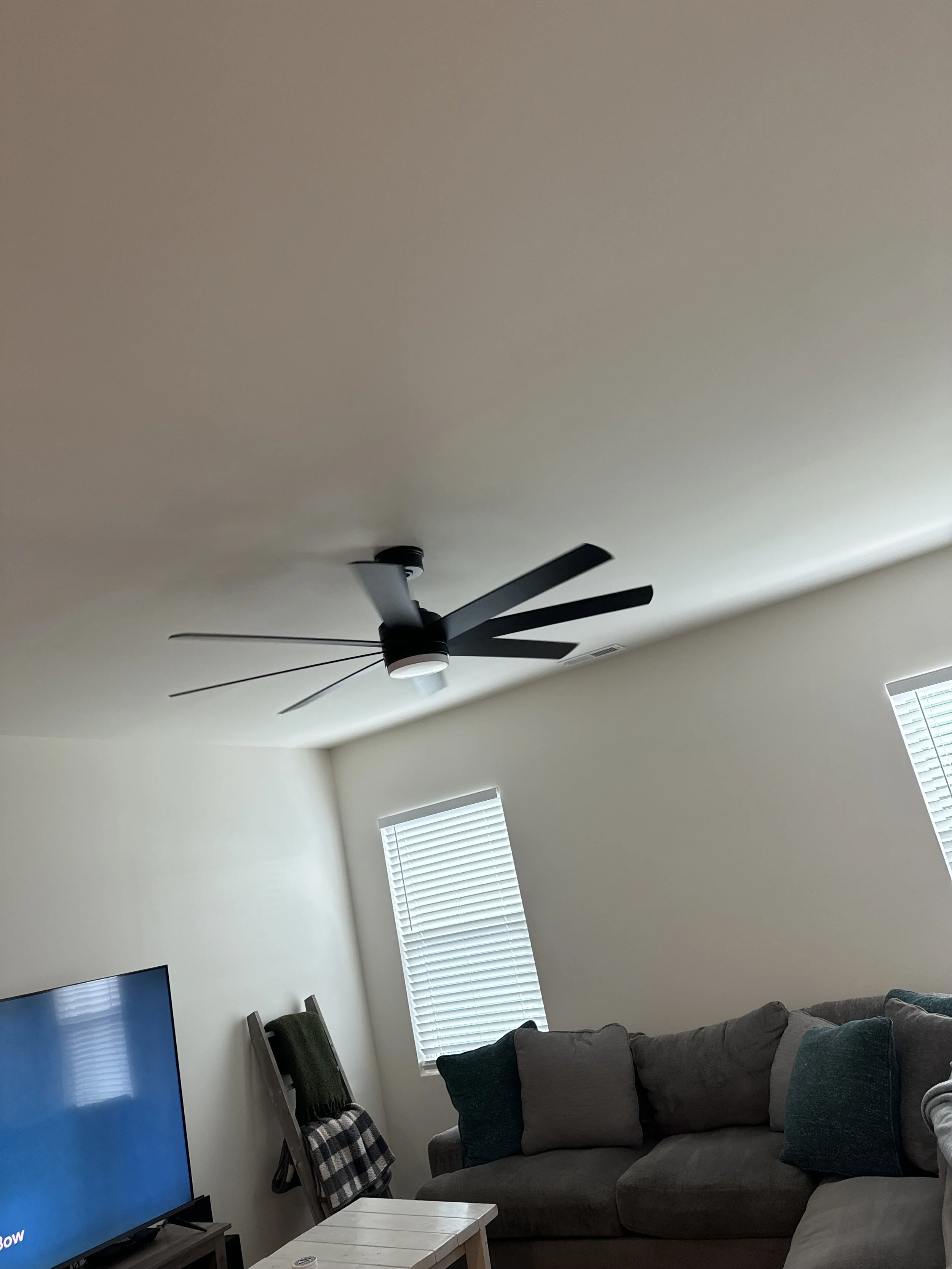 Living room with a ceiling fan, a TV, a chair, and a couch with pillows. Two windows with blinds.