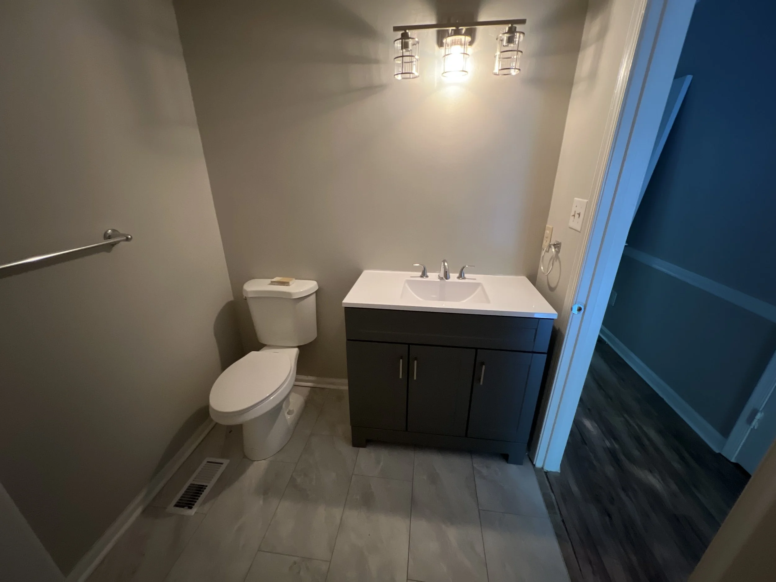 Small bathroom with a toilet, a dark vanity with a sink, and a wall-mounted light fixture above.