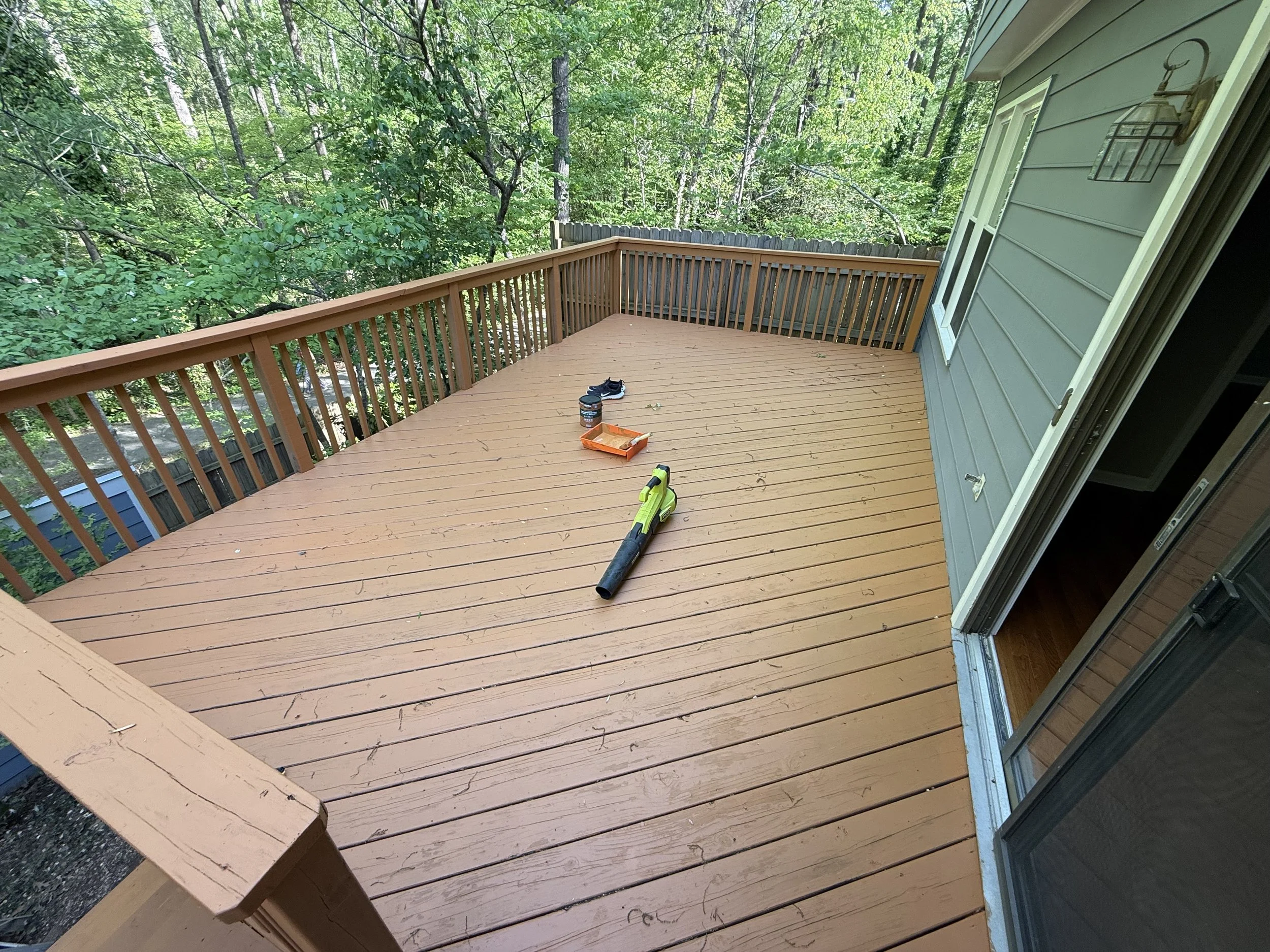 Empty outdoor wooden deck with some tools and shoes, surrounded by trees and greenery.