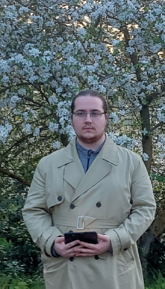 A young man standing in front of a flowering tree holding a smartphone.