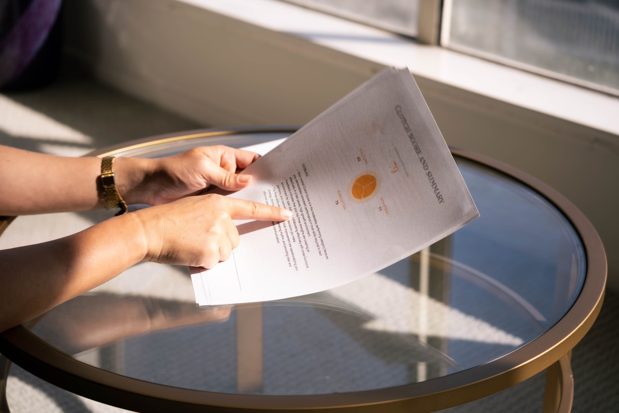 A person is holding and reading a document with a pie chart on a small round table near a window.
