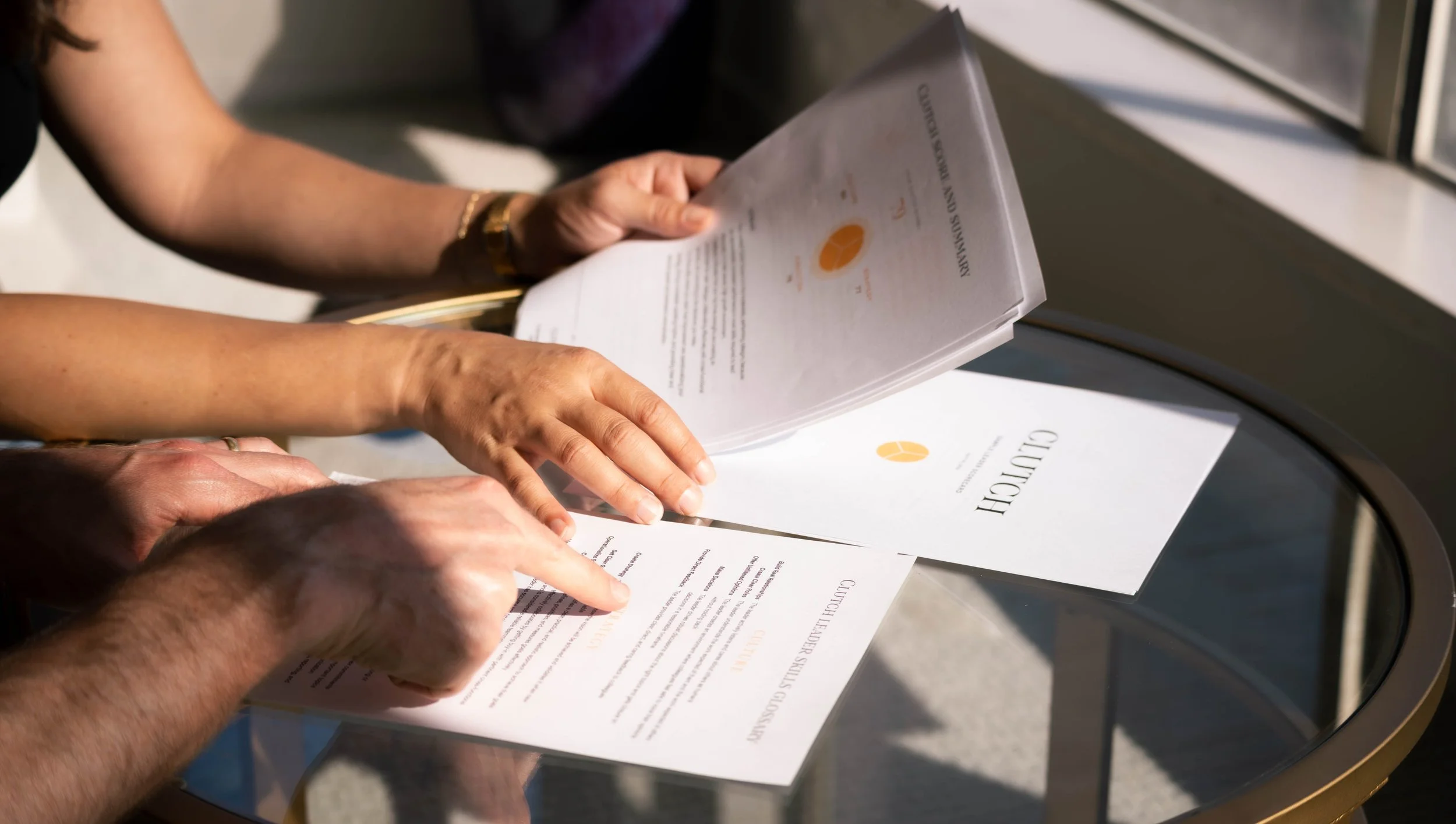 Two people examining a printed menu or brochure with a glass top table underneath, during daytime.