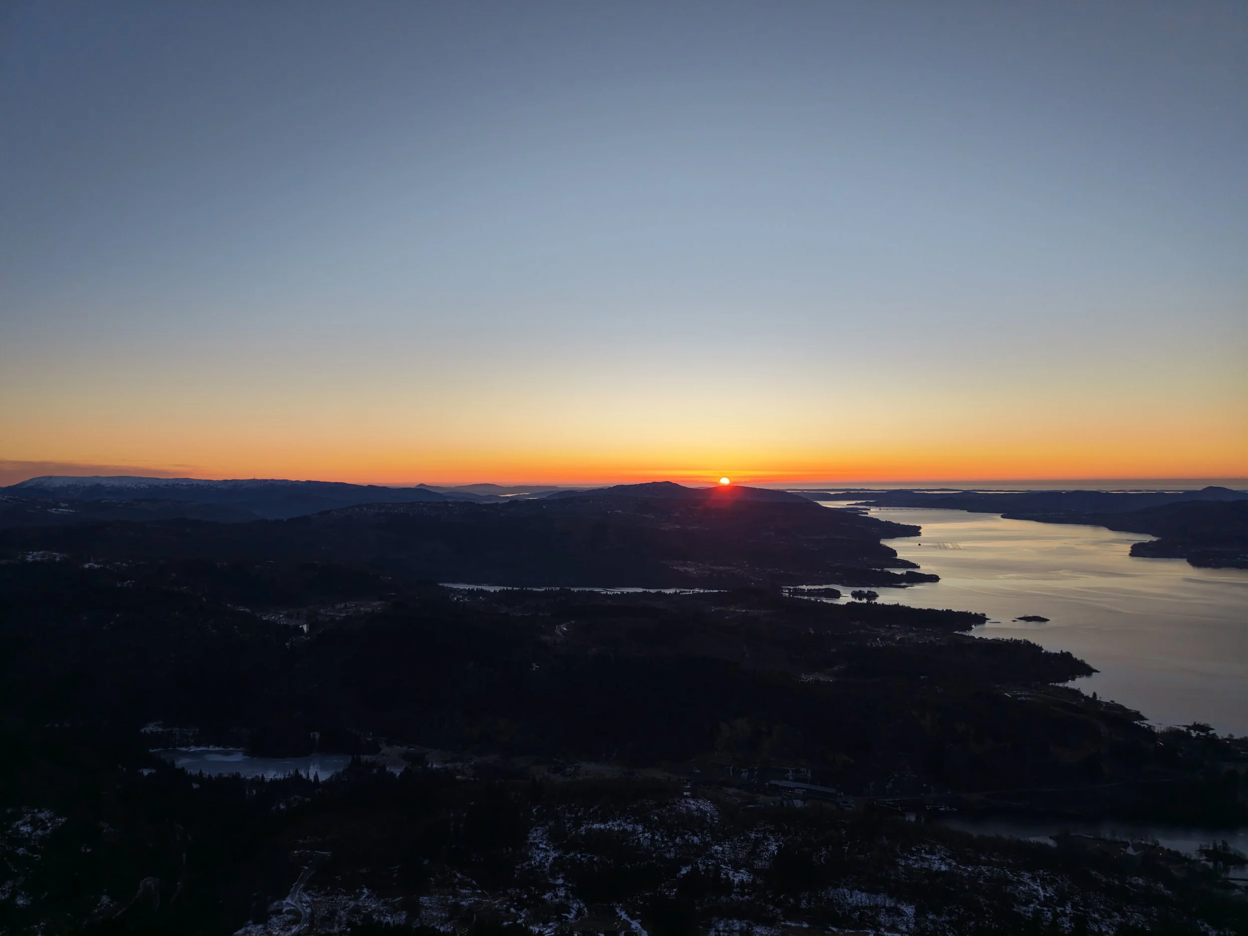 Sunset over a body of water with hills and mountains in the distance.