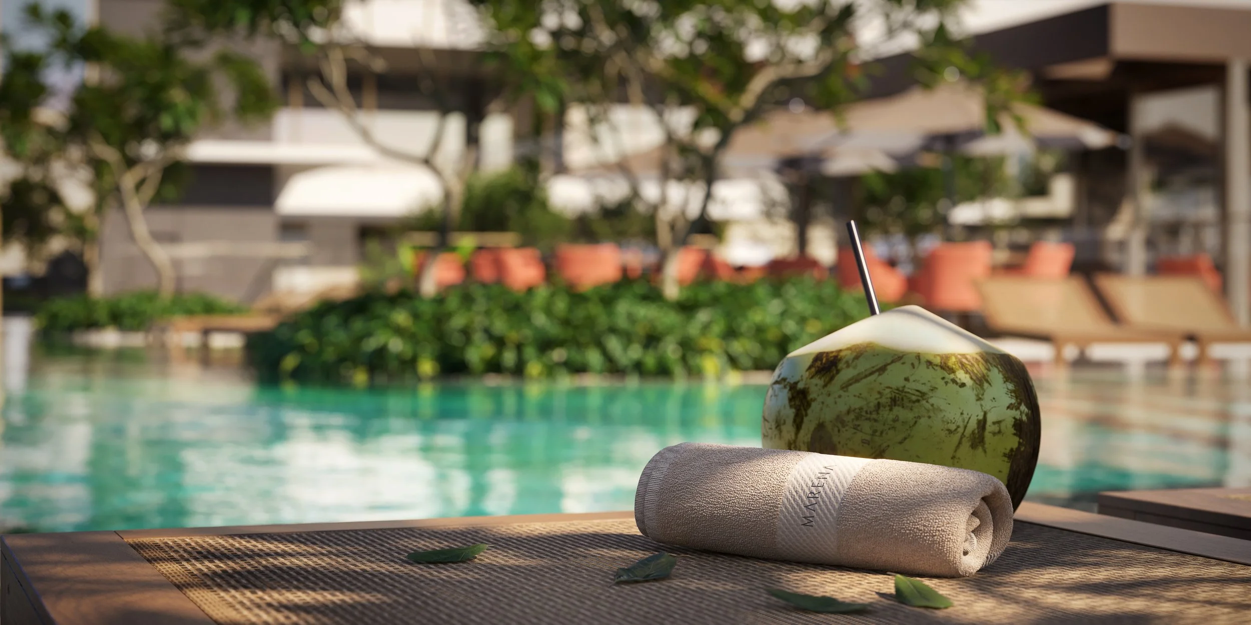 Cocoadeira de água de coco com canudo, toalha branca e folhas na borda de uma piscina ao ar livre.