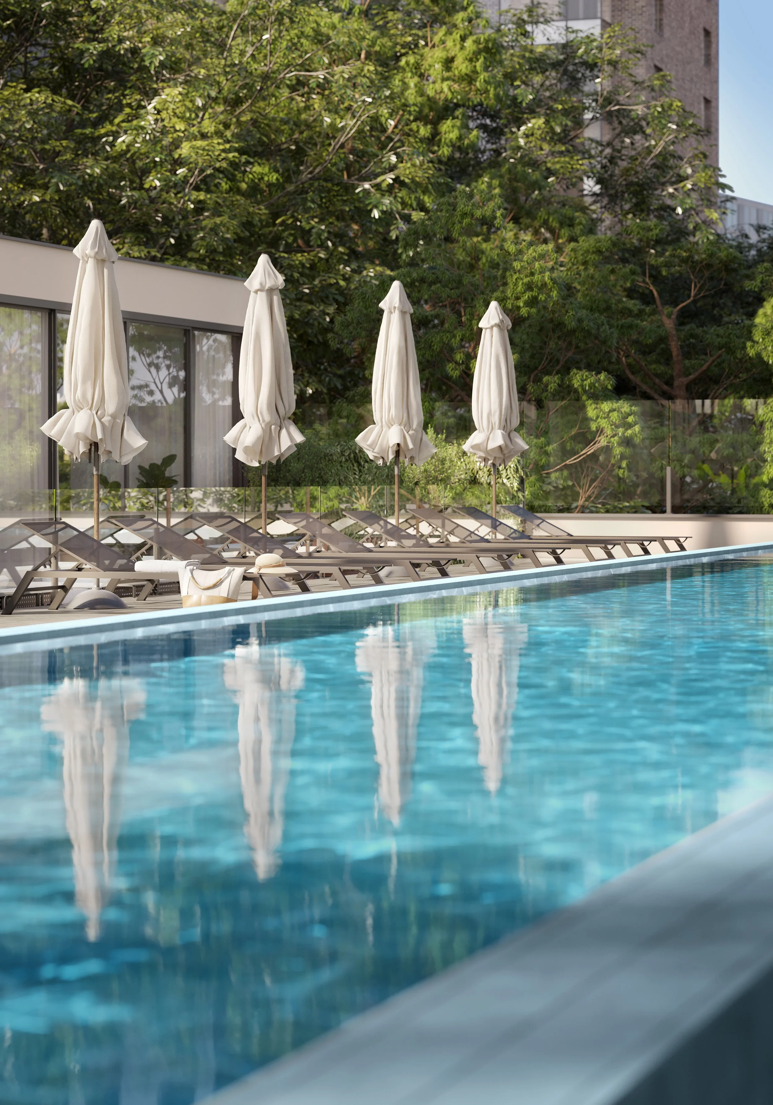 Piscina ao ar livre com espreguiçadeiras e guarda-sóis brancos, cercada por árvores verdes e uma cerca de vidro, em um dia ensolarado.