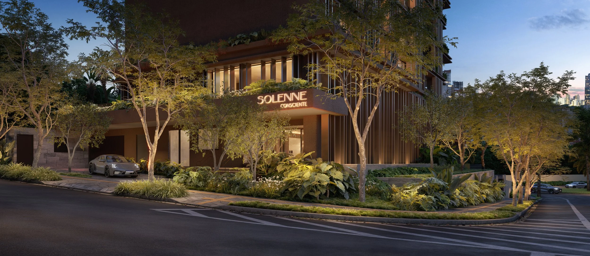 Edifício moderno com fachada de vidro, rodeado por árvores verdes e plantas, com um carro estacionado na rua em frente ao edifício à noite.