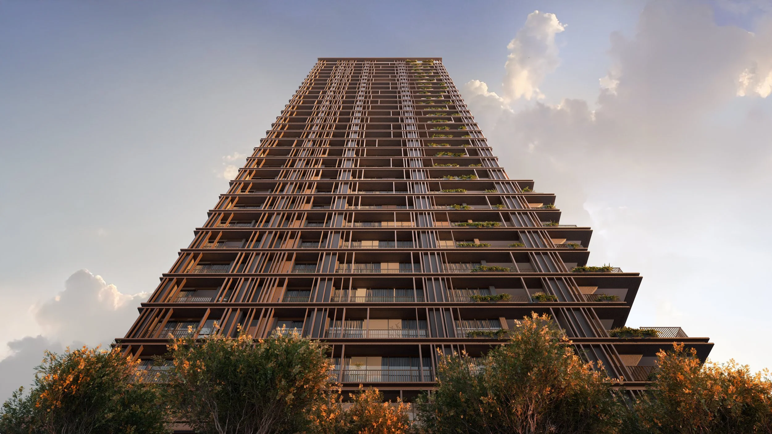Edifício alto com fachadas de vidro e estruturas de metal, vista de baixo para cima, com árvores na frente, céu com nuvens ao fundo.