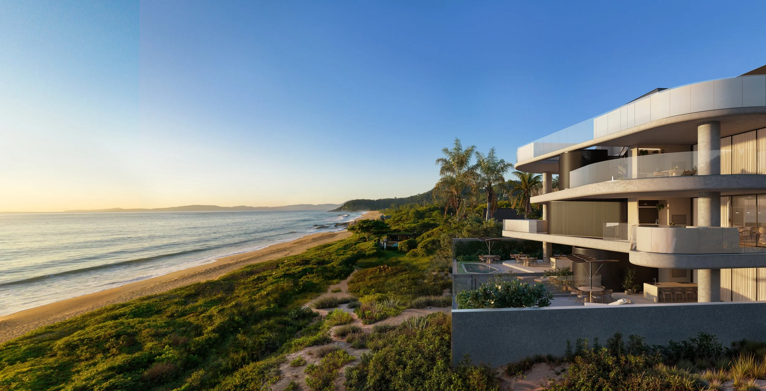 Prédio moderno com varandas voltadas para a praia do Estaleiro, ao lado de uma vegetação de jardim, com vista para o mar ao entardecer.