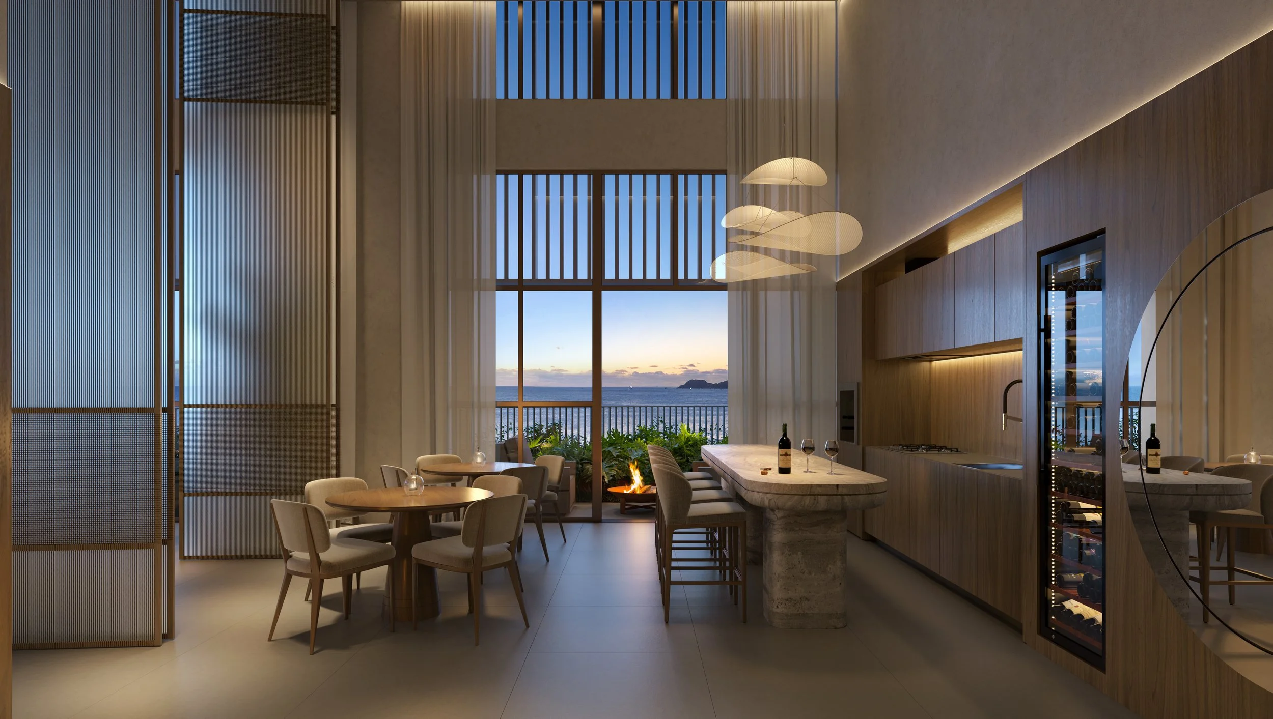 Sala de jantar e cozinha com vista para o mar ao pôr do sol, móveis modernos de madeira, mesa de jantar, cadeiras estofadas, ilha de cozinha com garrafas de vinho e taças, parede de vidro aberta para o terraço com plantas e fogo ao ar livre.