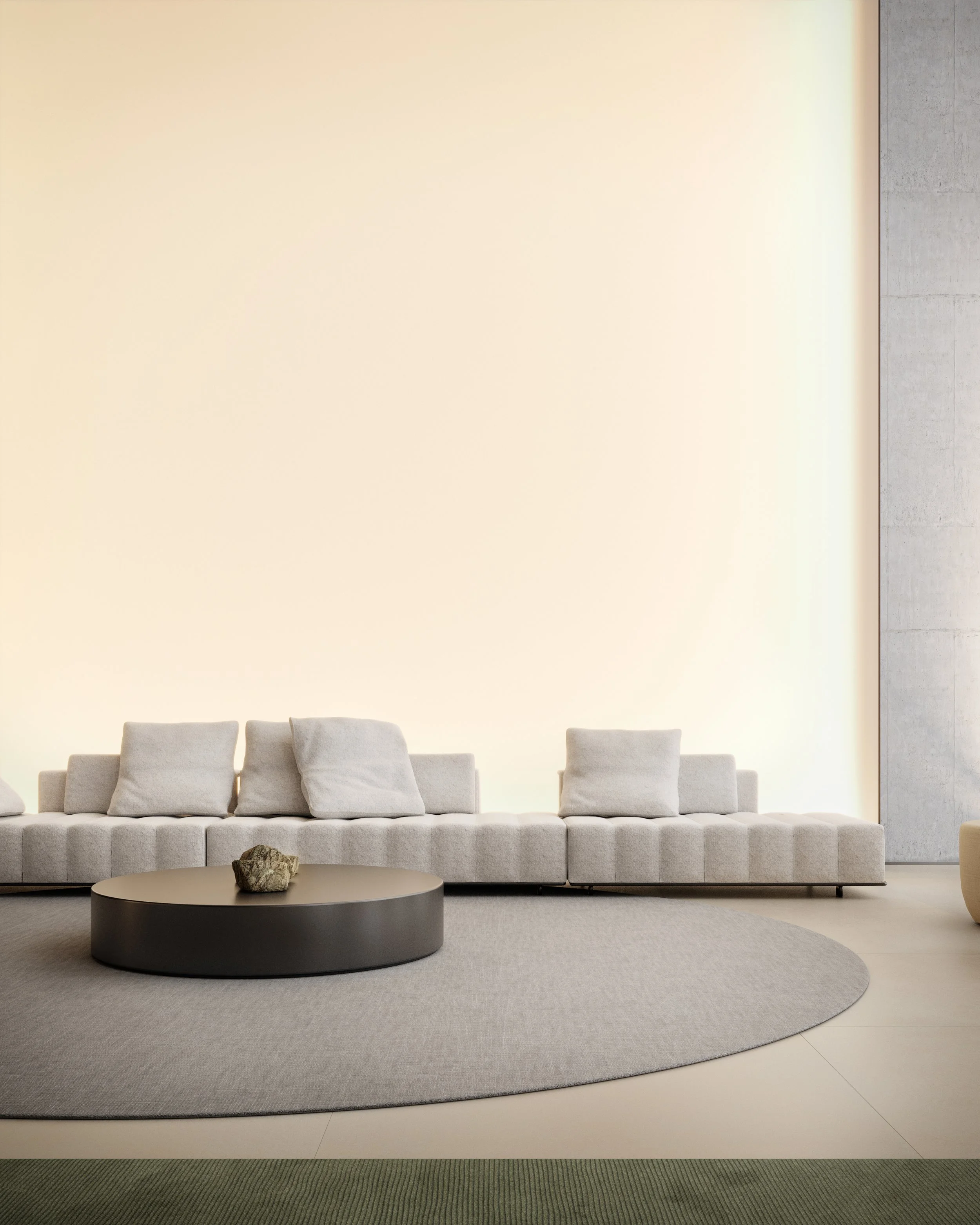 Sofá cinza claro com almofadas, mesa de centro preta com pedra, tapete circular cinza claro e iluminação suave na parede ao fundo.