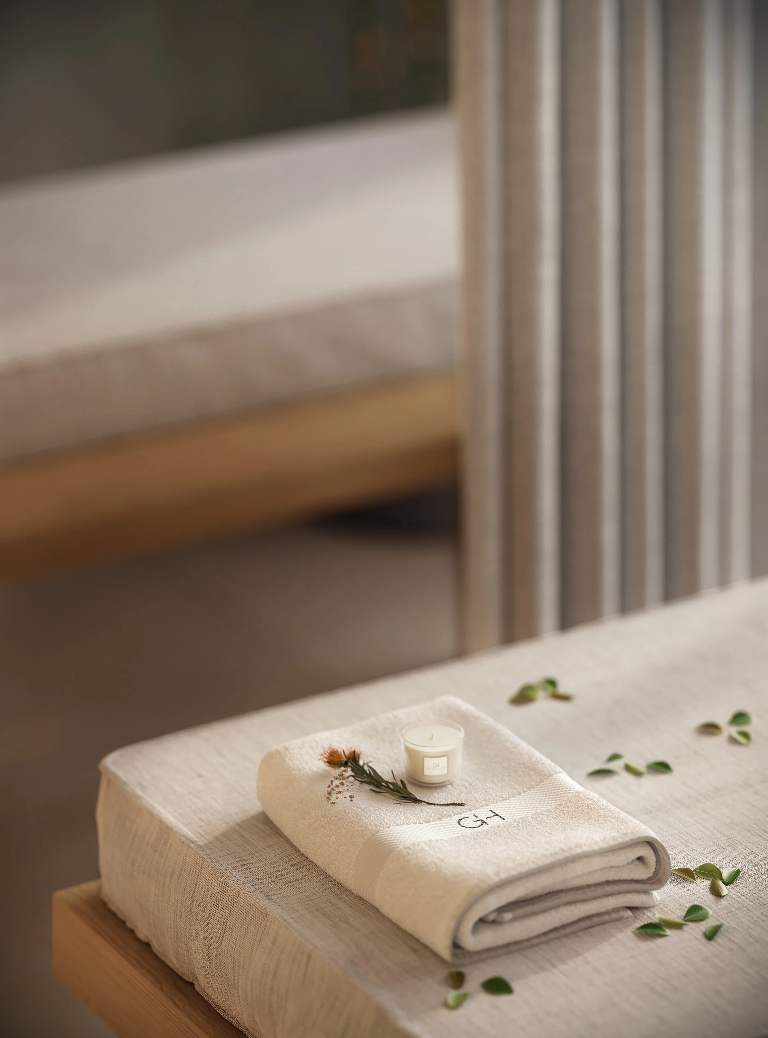 Toalha branca dobrada com monograma G+H, velas brancas e folhas verdes decorativas em uma mesa