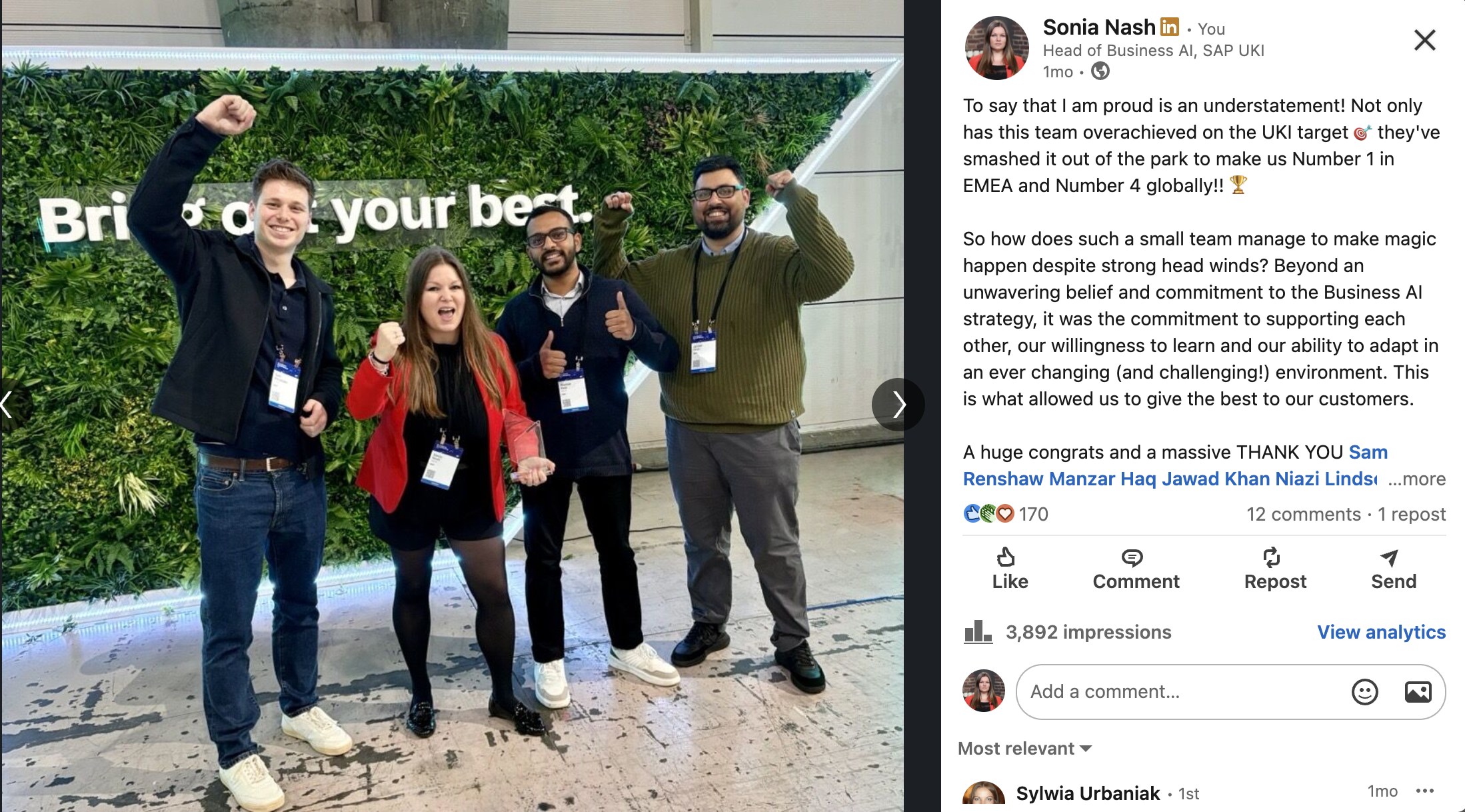 Group of four people standing in front of a green wall with a sign that says "Bring out your best." They are smiling and cheering, with several of them raising their fists or giving thumbs up. The group appears happy and celebratory.