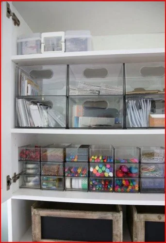 Storage cabinet with clear plastic bins containing papers and craft supplies like pom-poms and beads.