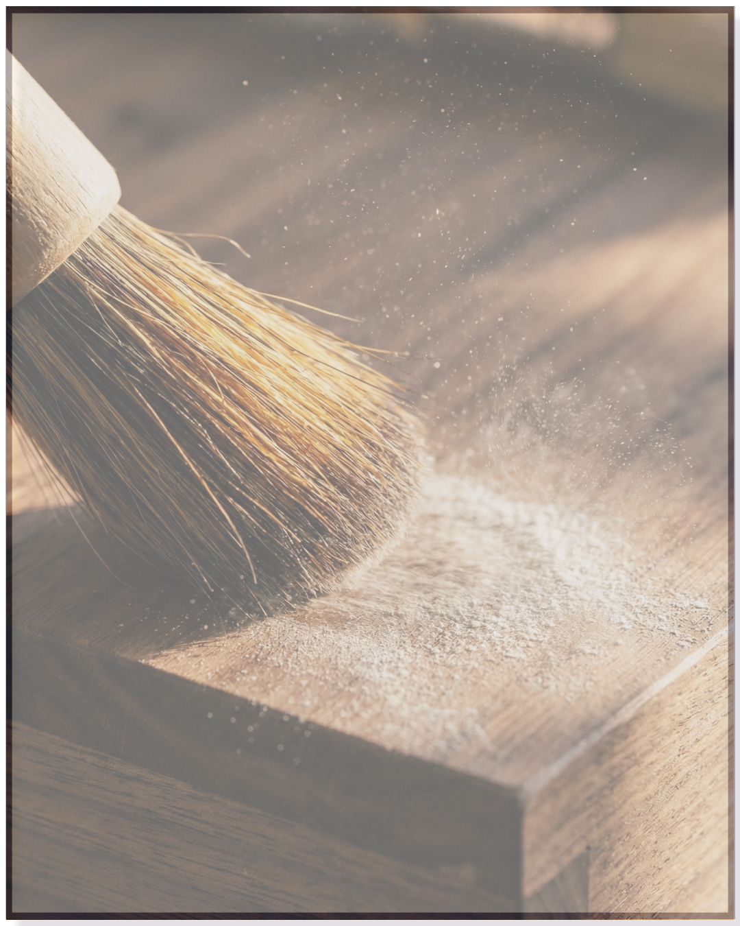 Close-up of a paintbrush dusting a wooden surface with white powder