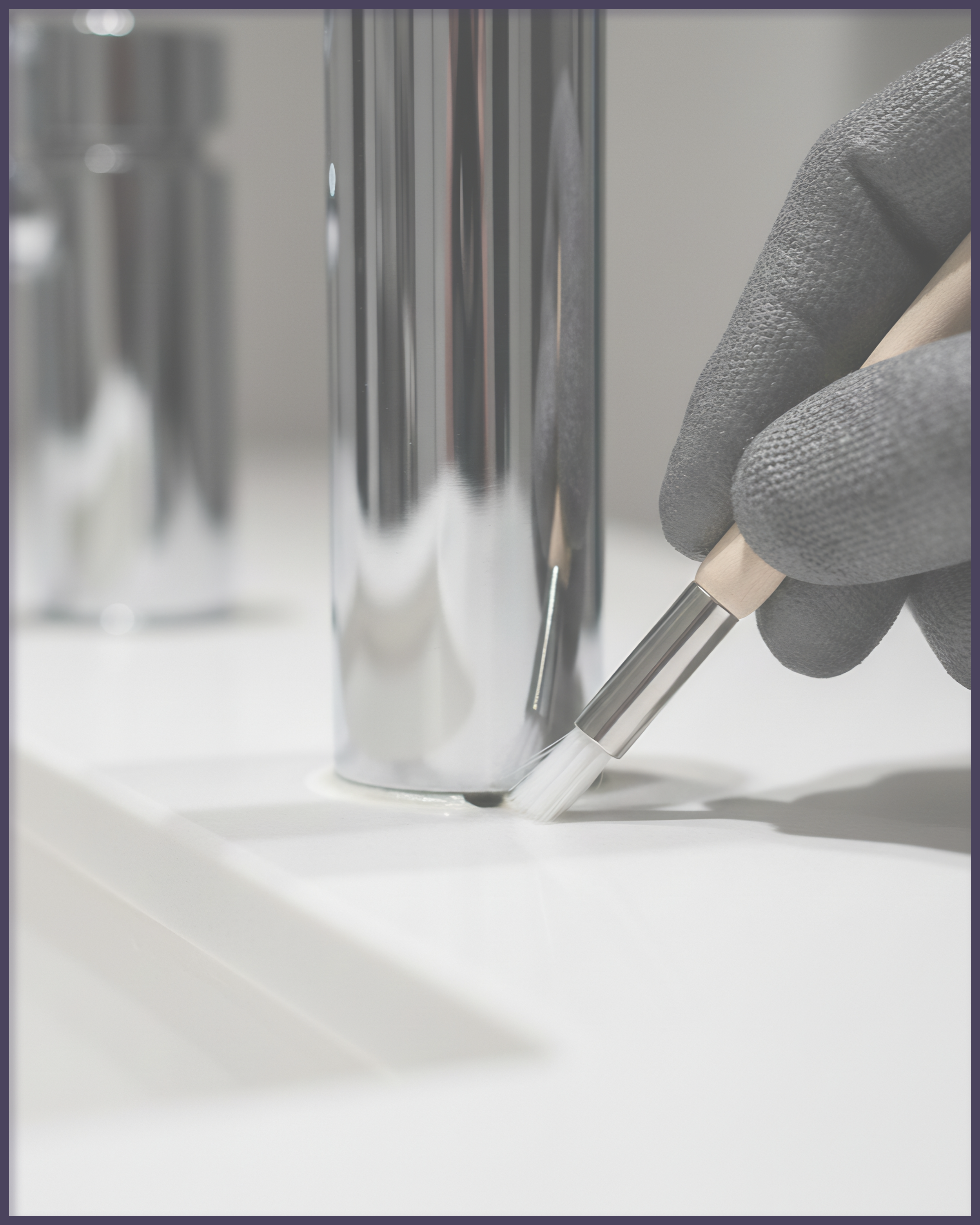 A hand in a gray glove holding a precision tool near a shiny metal container on a white surface.
